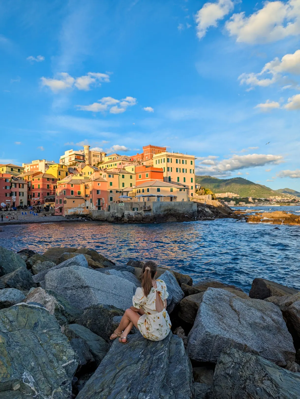 Woman sitting on the rocks facing the colourful houses of the fishing village