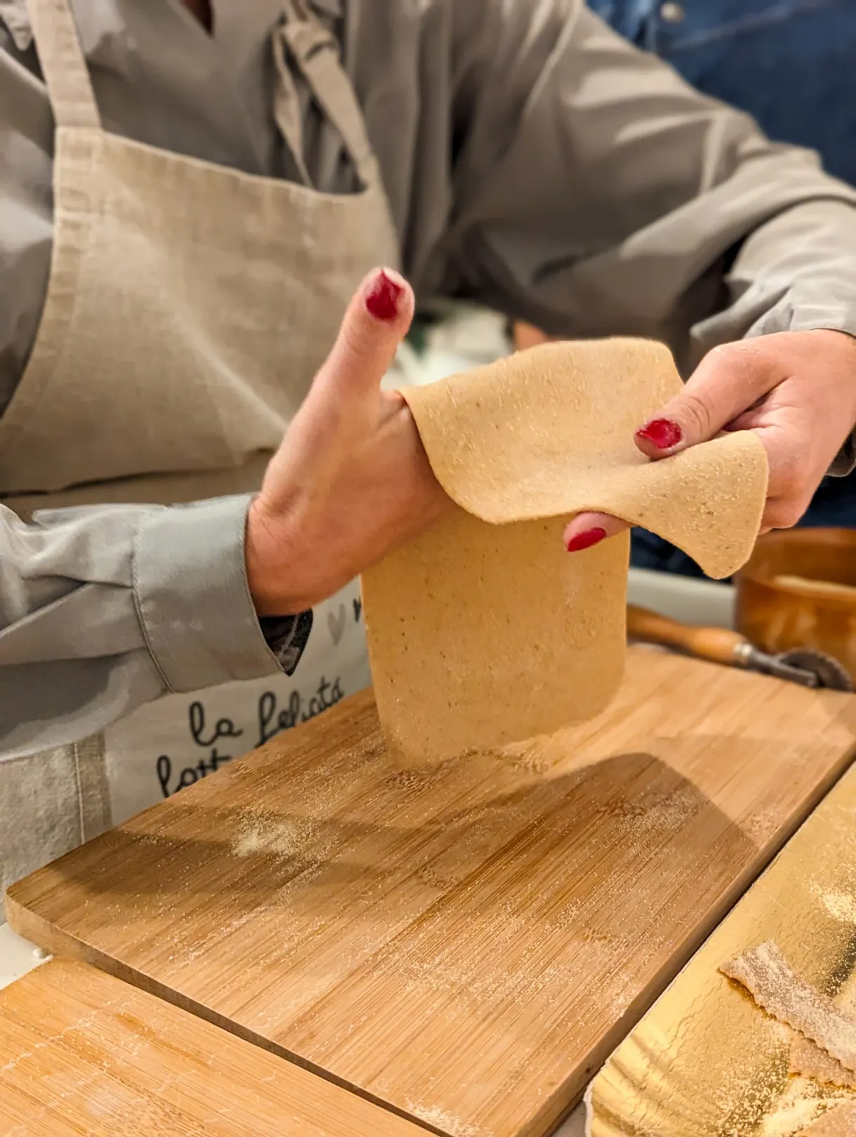 Sheet of fresh pasta stretched by hand above a board