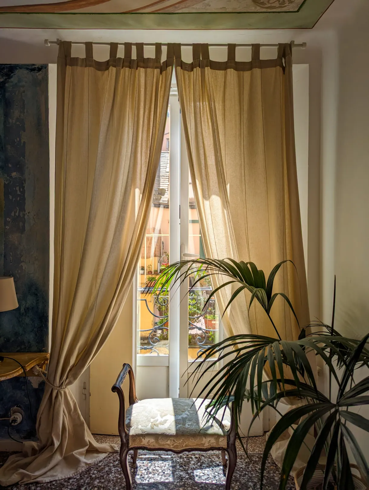 Tall window with beige curtains and a potted palm