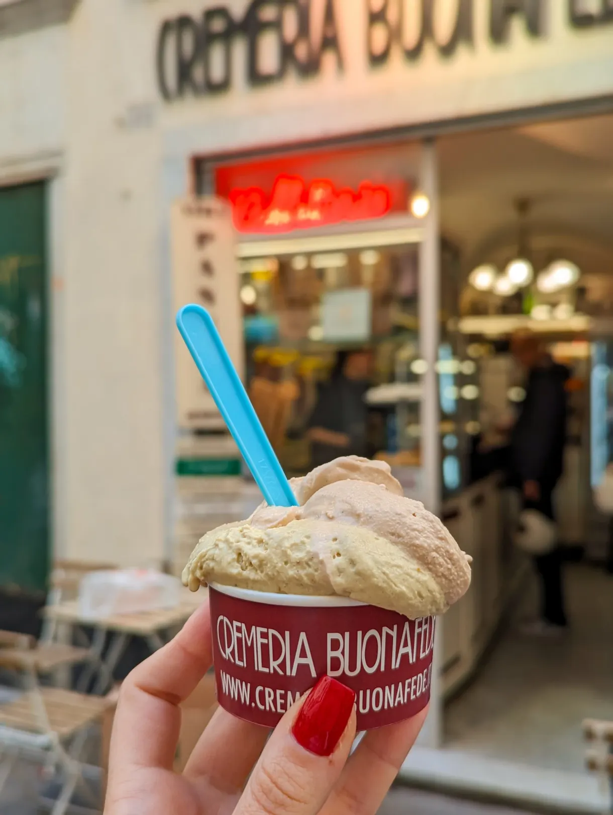 Tub of ice cream held in the hand in front of a gelateria window