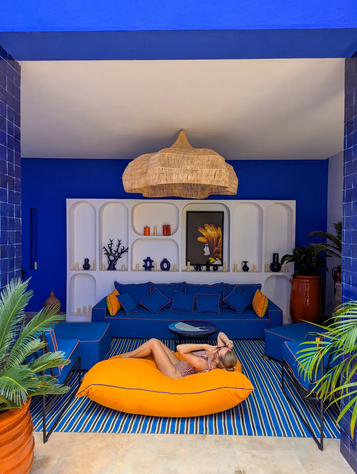 Blue lounge of a riad in Marrakech, Marie lying on a big orange pouf
