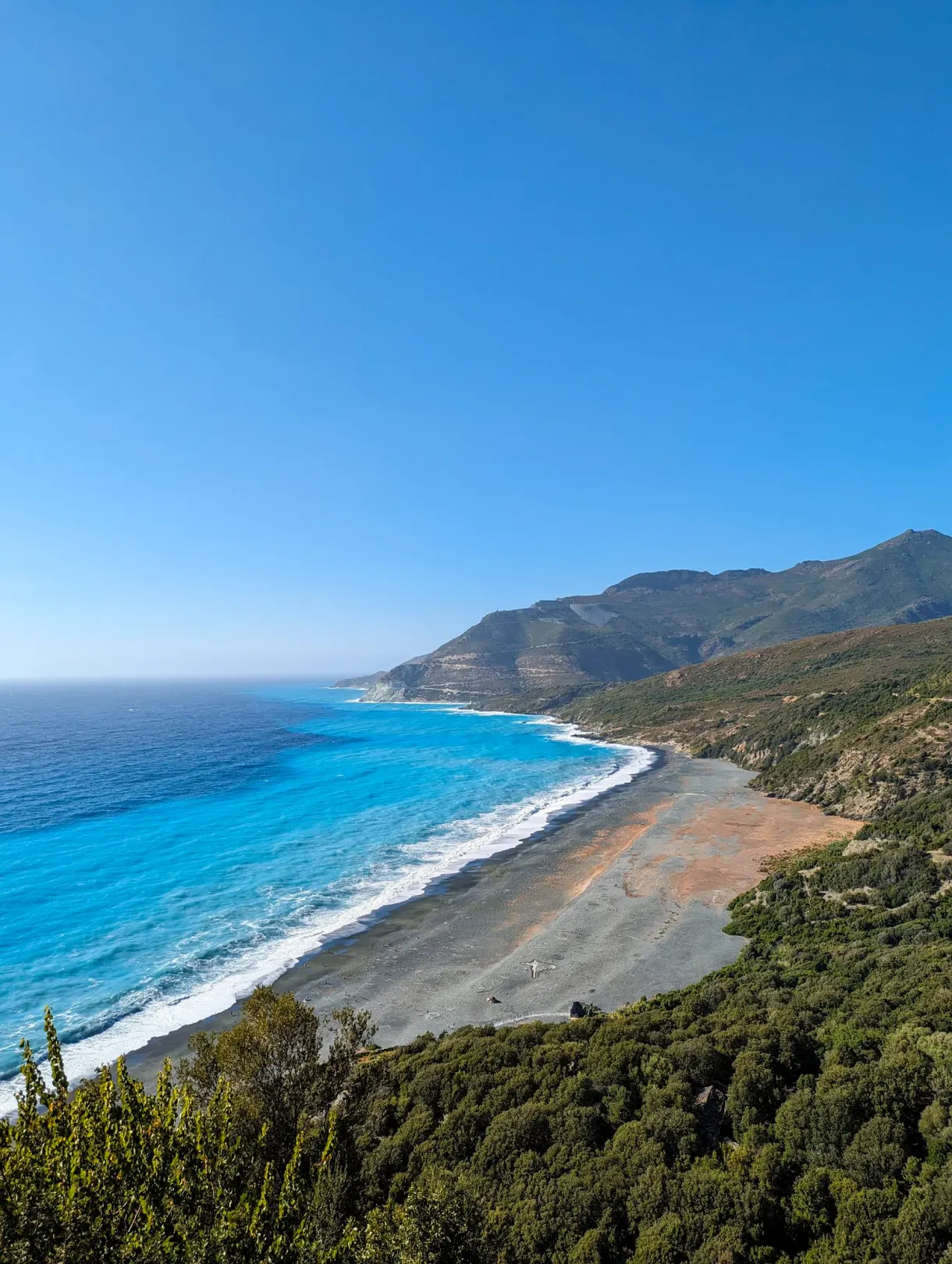 Pebble beach and turquoise water at the foot of the Corsican mountains