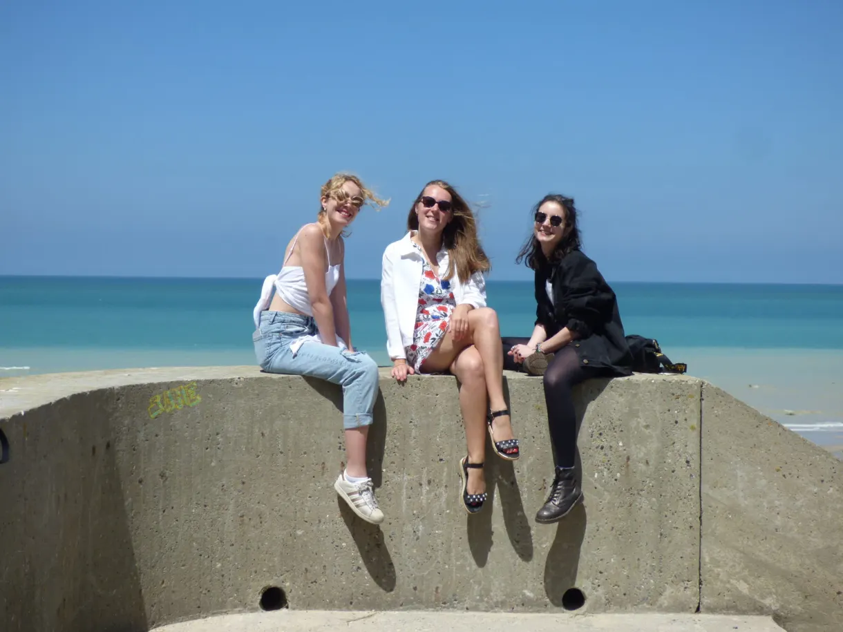 Three friends sitting on a block of concrete facing the sea