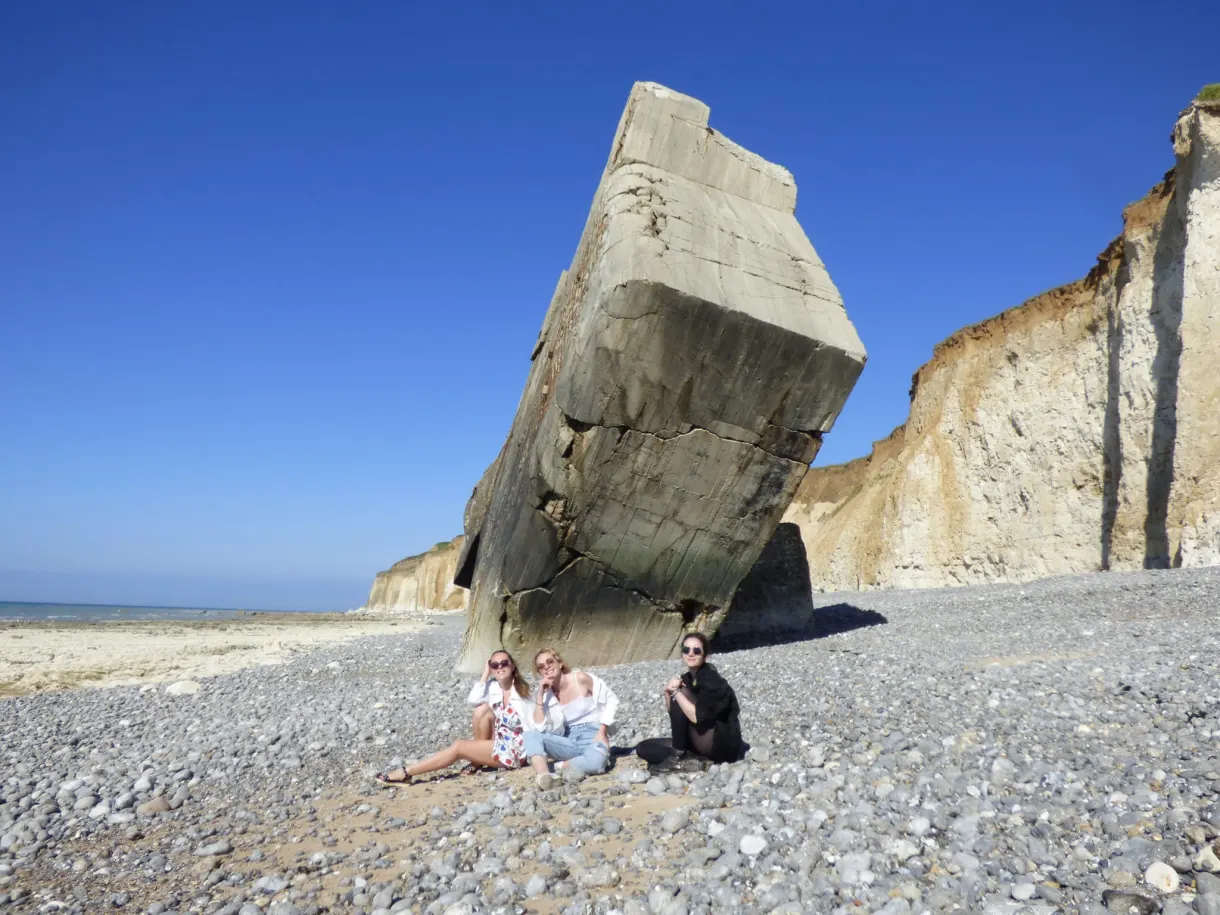 Three friends sitting under a tipped-over bunker on the beach