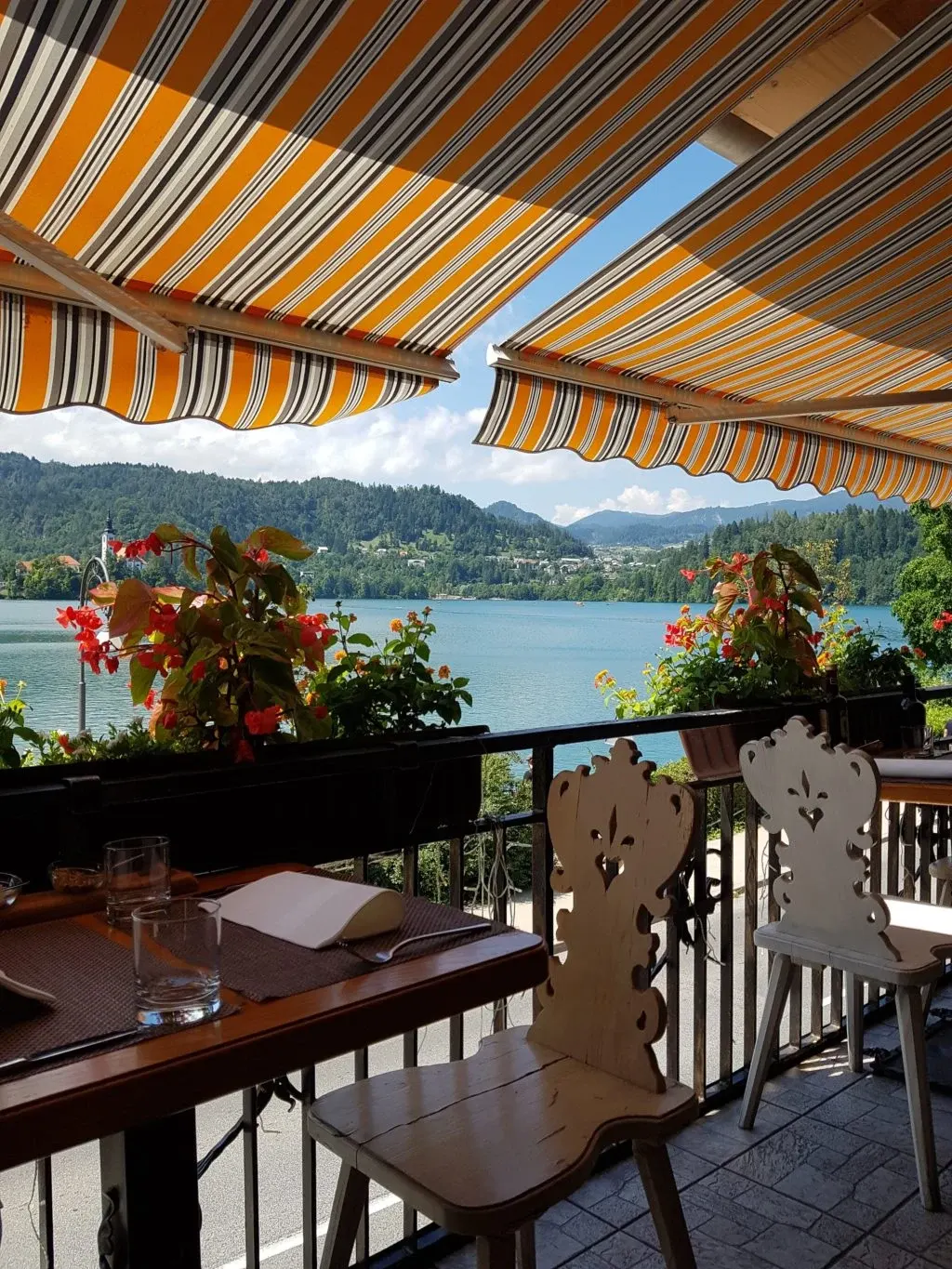 Flower-decked terrace beneath a striped awning facing the lake