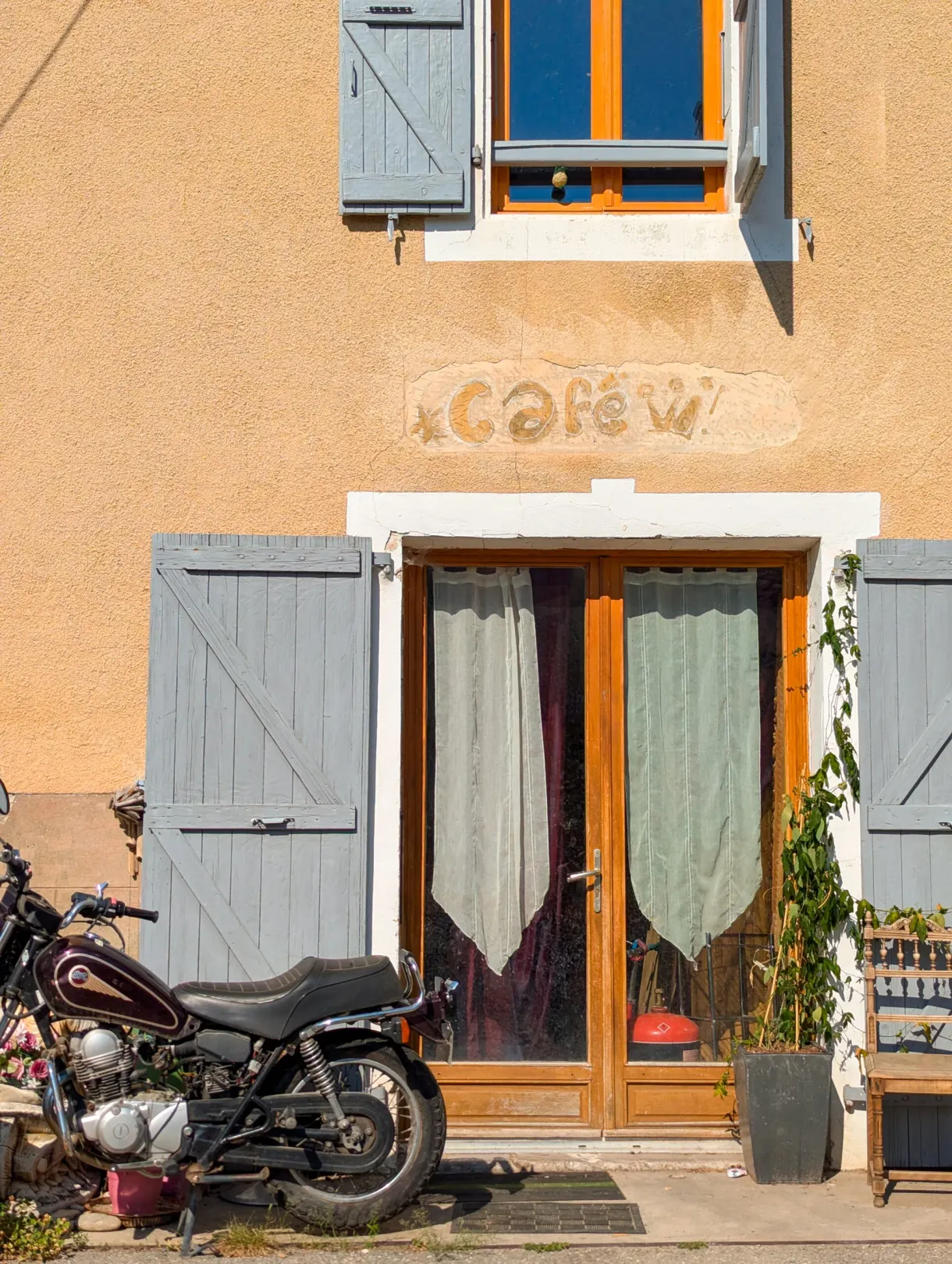 Old cafe sign painted on an ochre facade, motorbike parked in front