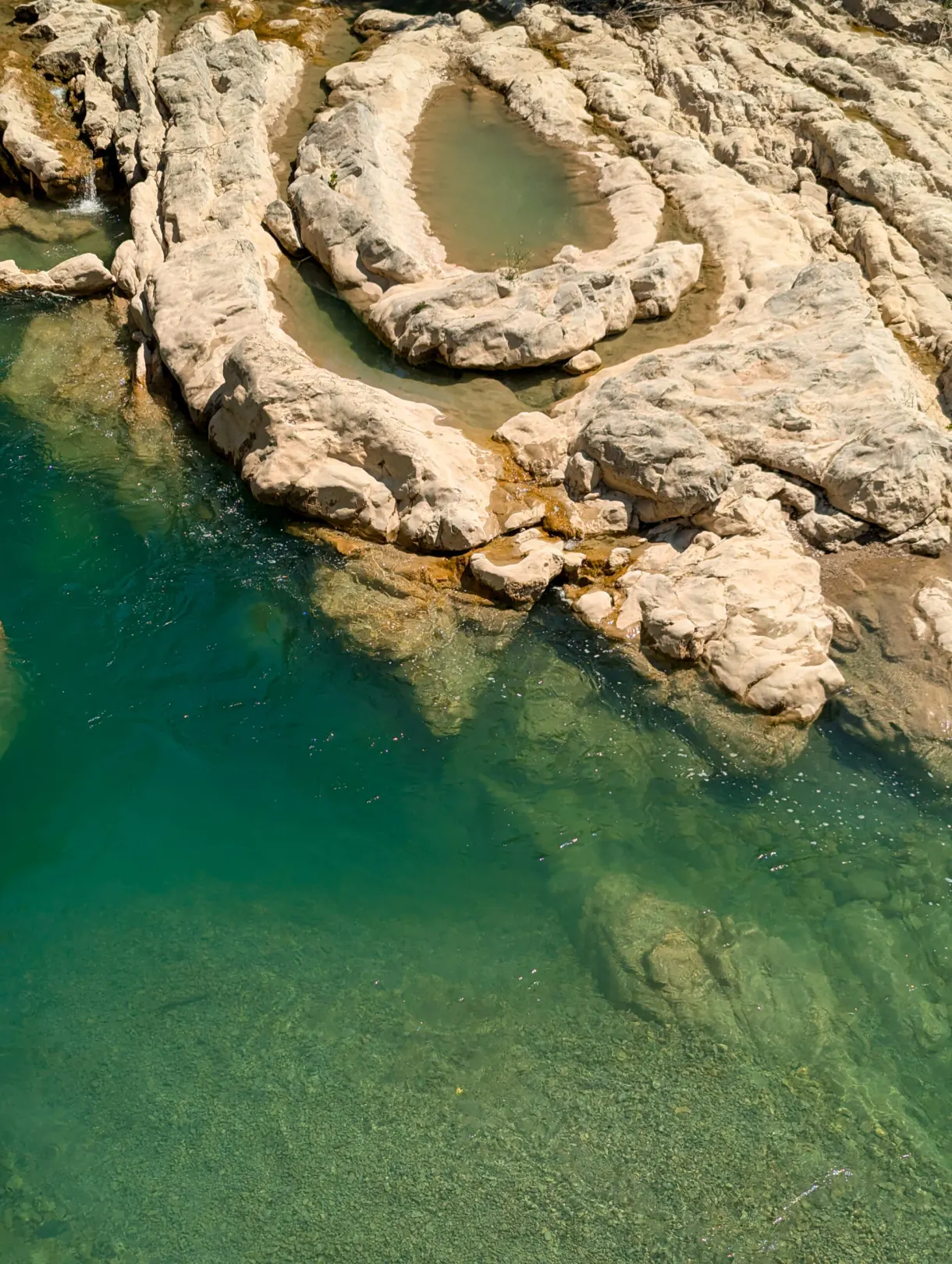 Circular basin of white rock at the edge of emerald water