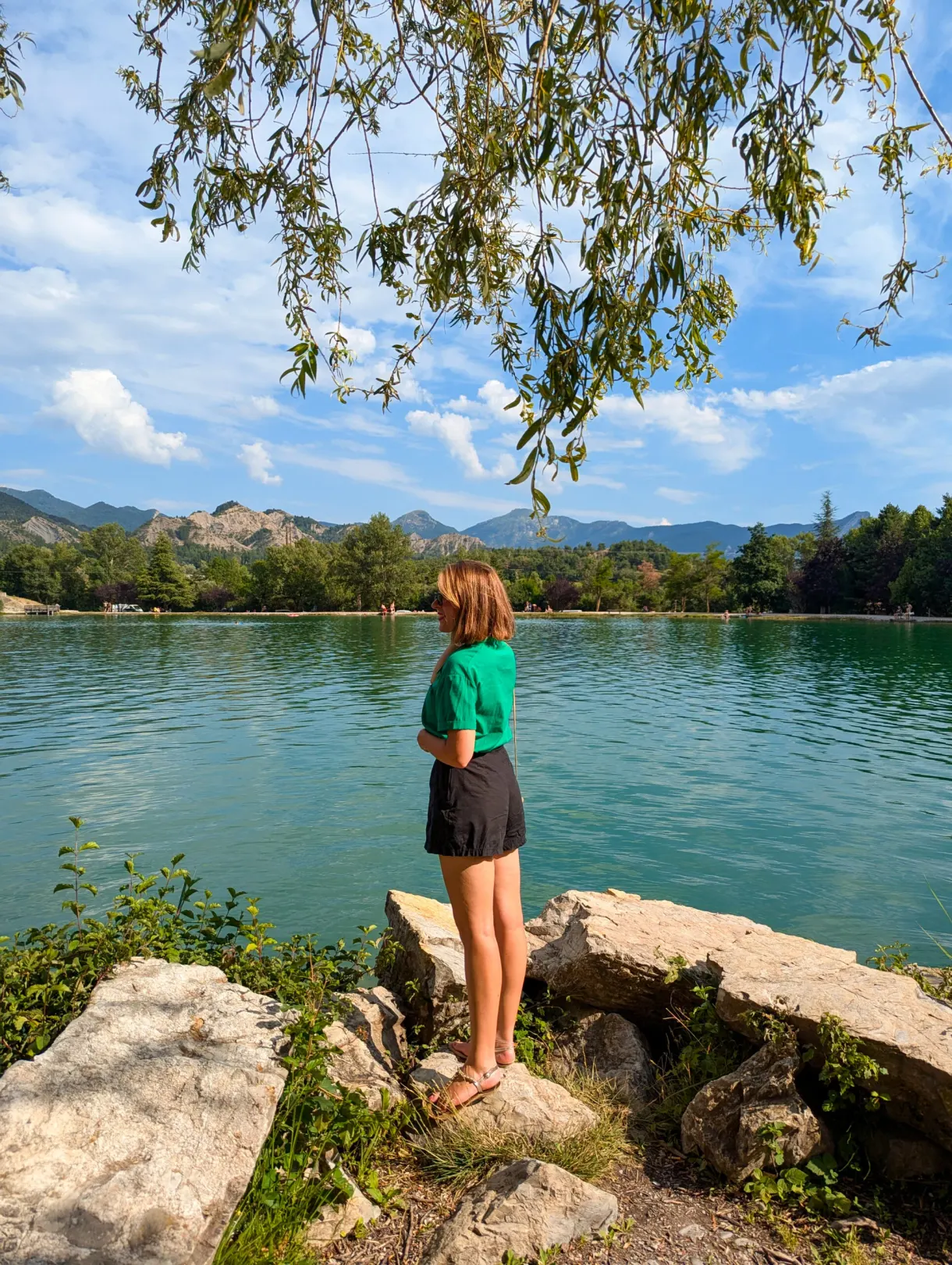 Woman walking at the edge of the lake under the branches of a willow