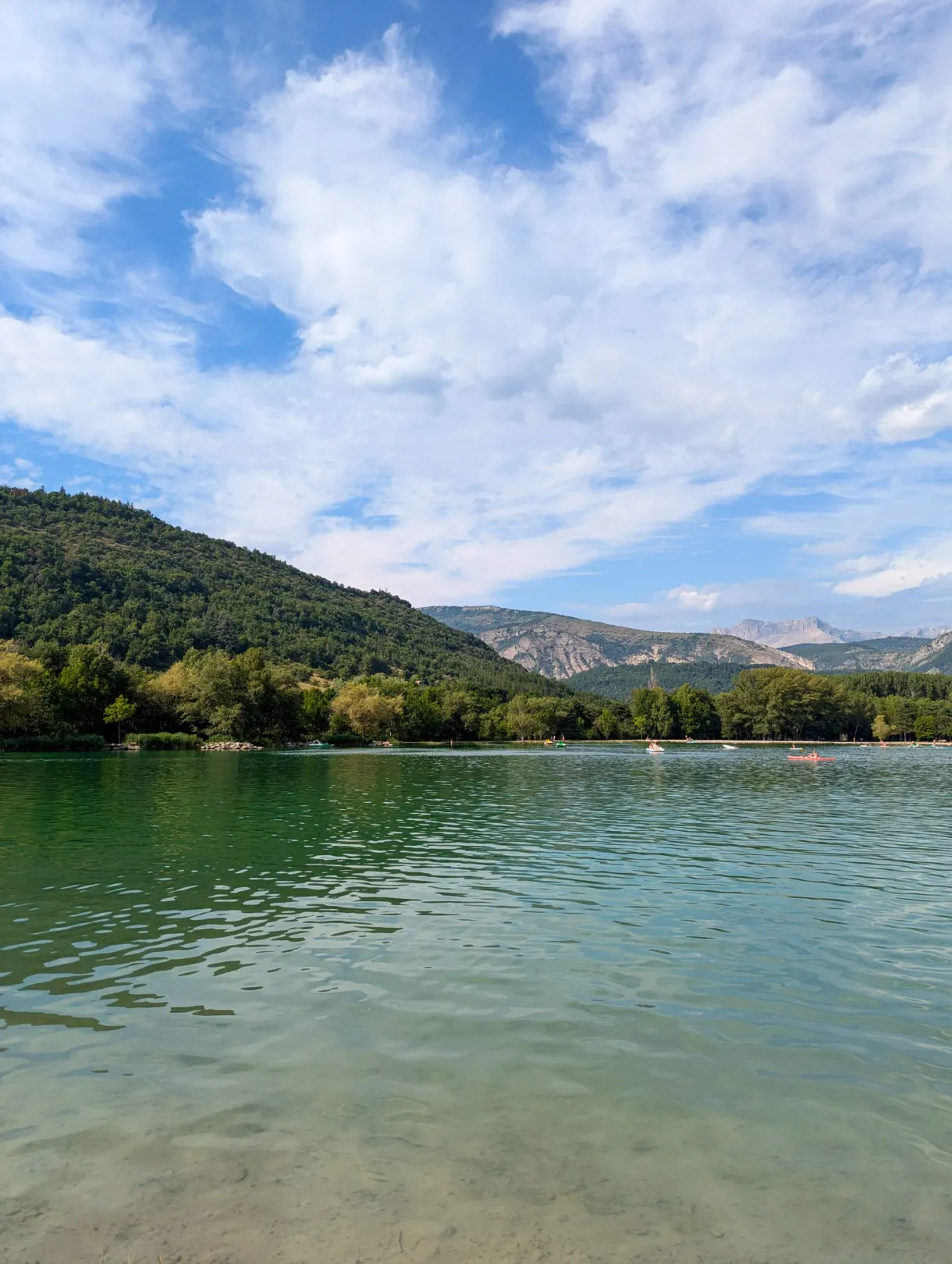 Calm lake and tree planted shore under a cloudy sky