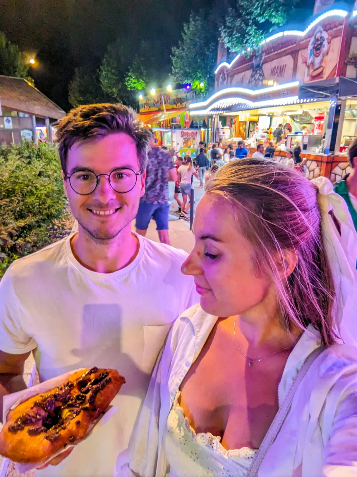 Couple sharing a pastry in front of the lit stalls of the festival