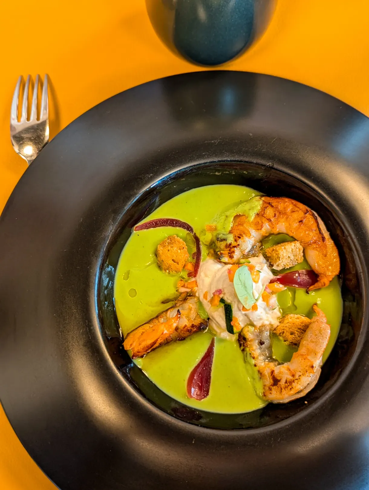 Pan fried prawns and green velouté served in a black bowl