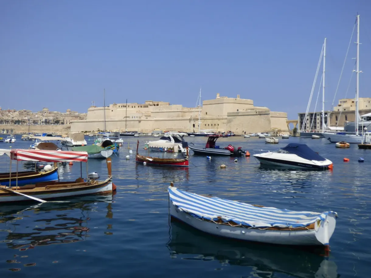 Colourful Maltese boats floating in front of the fortifications