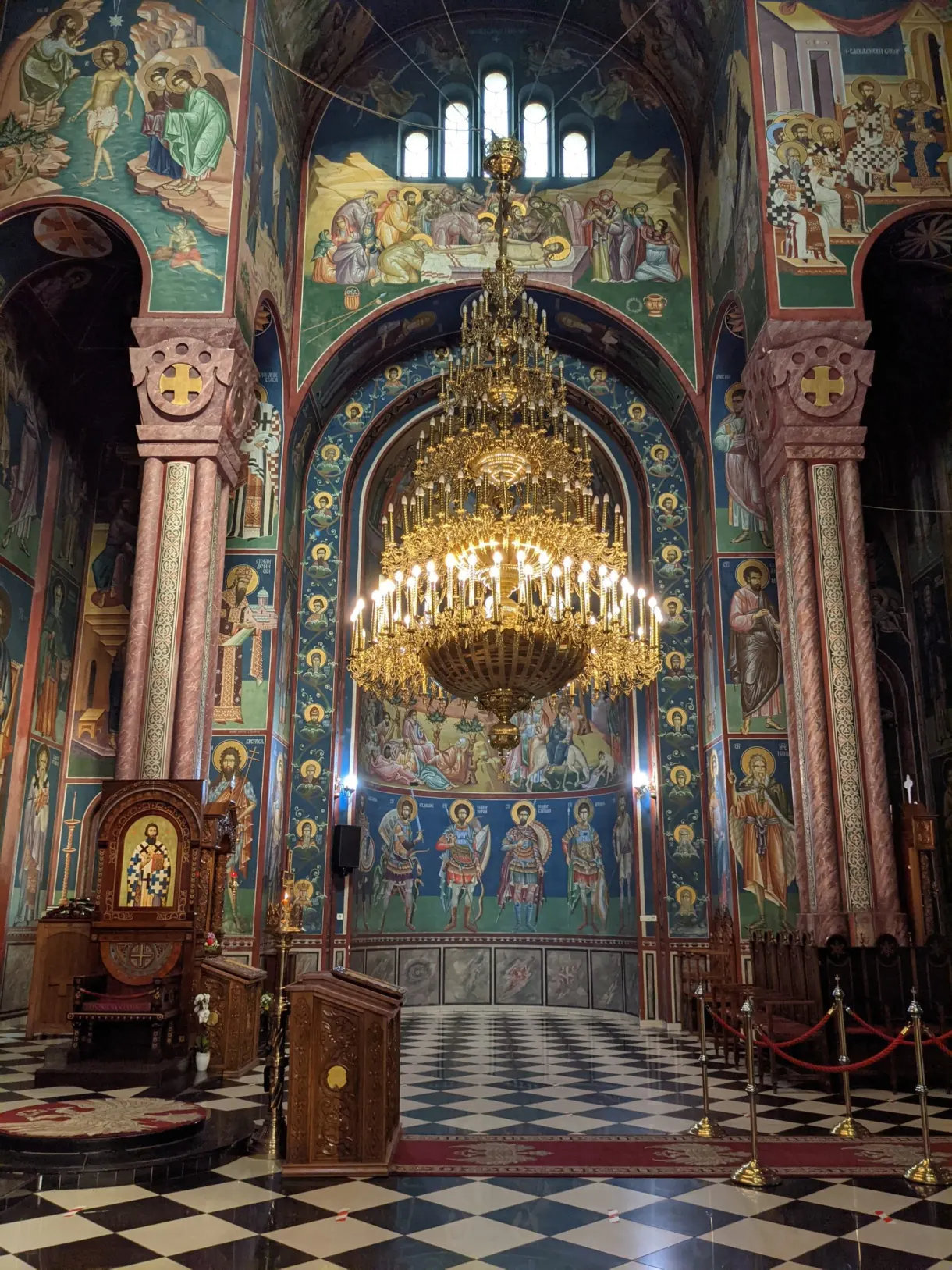 Golden chandelier and frescoes of an orthodox church with a chequered floor