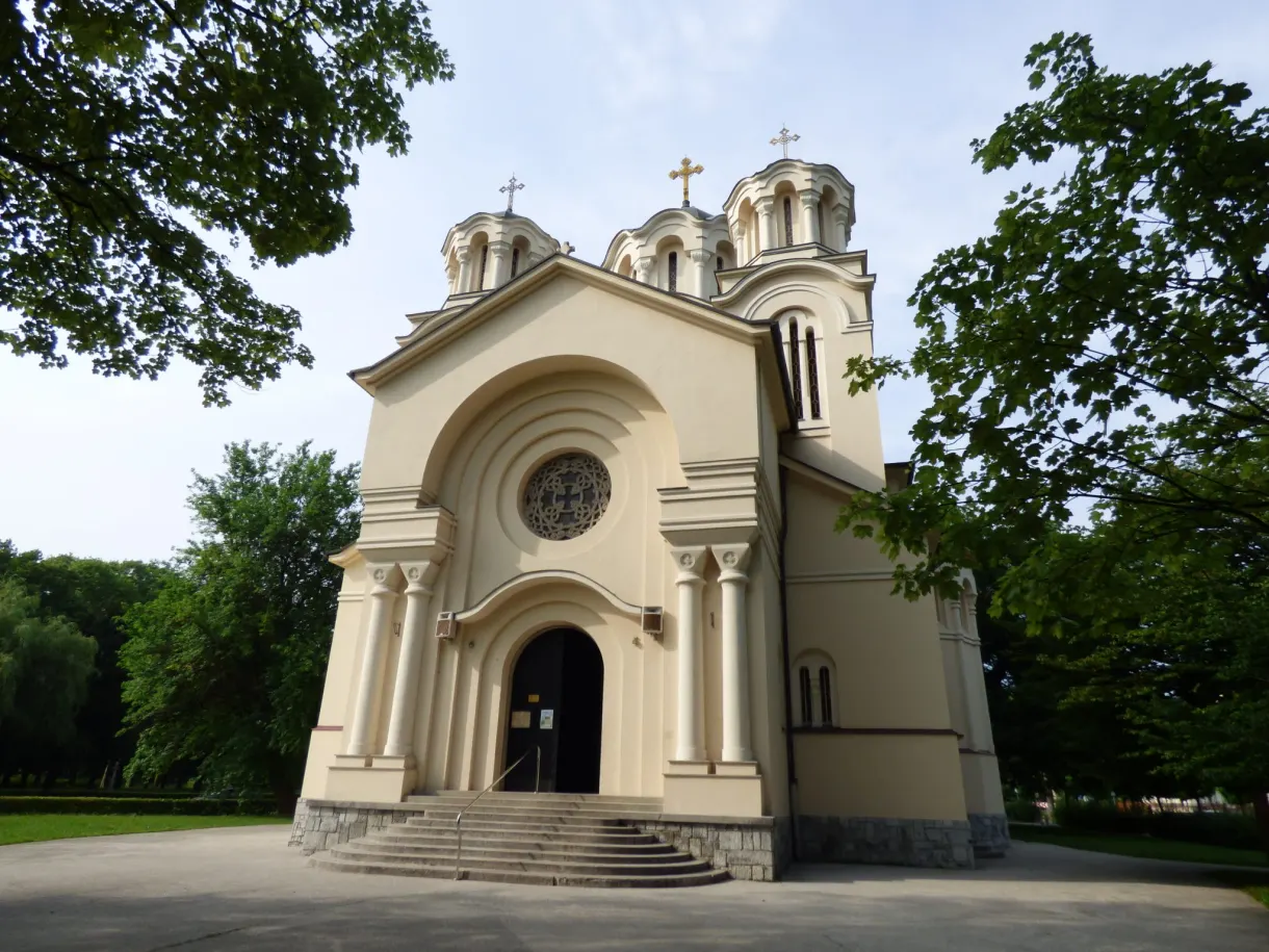 Cream orthodox church with three domes surrounded by trees