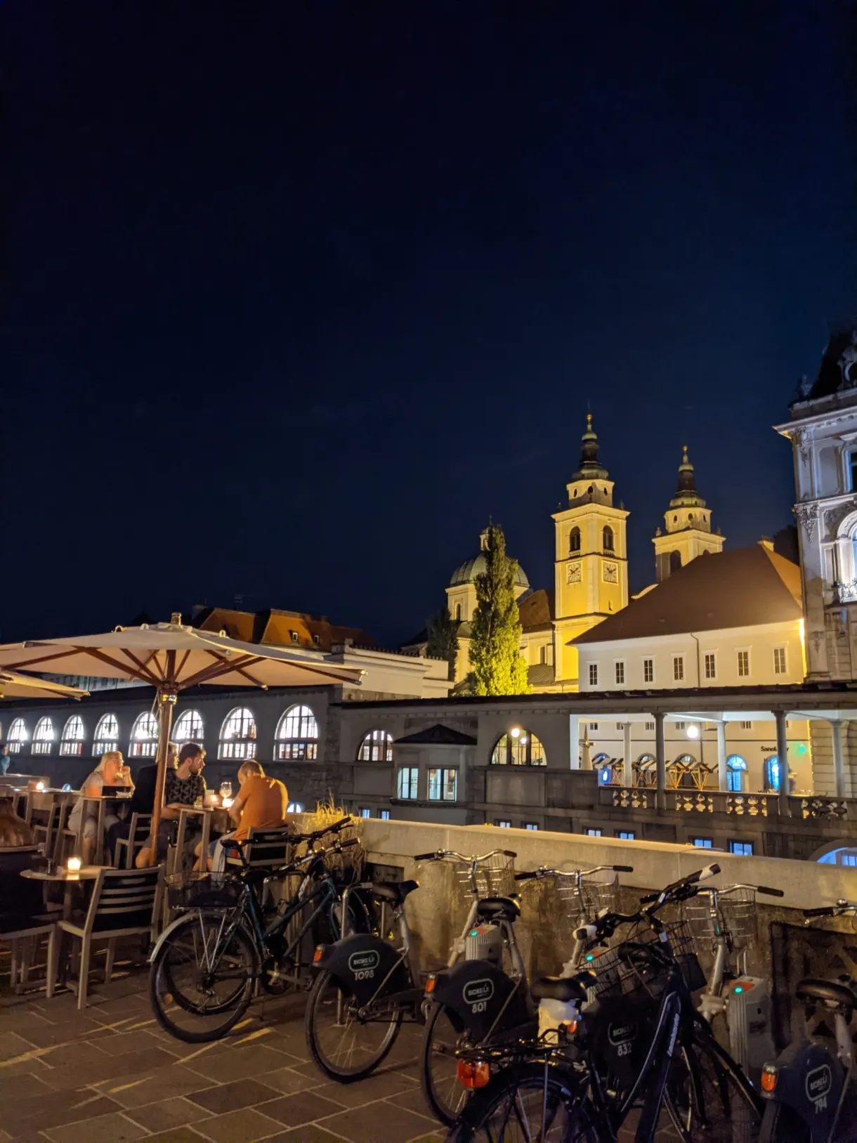 Bicycles and tables on the quay in front of the lit bell towers