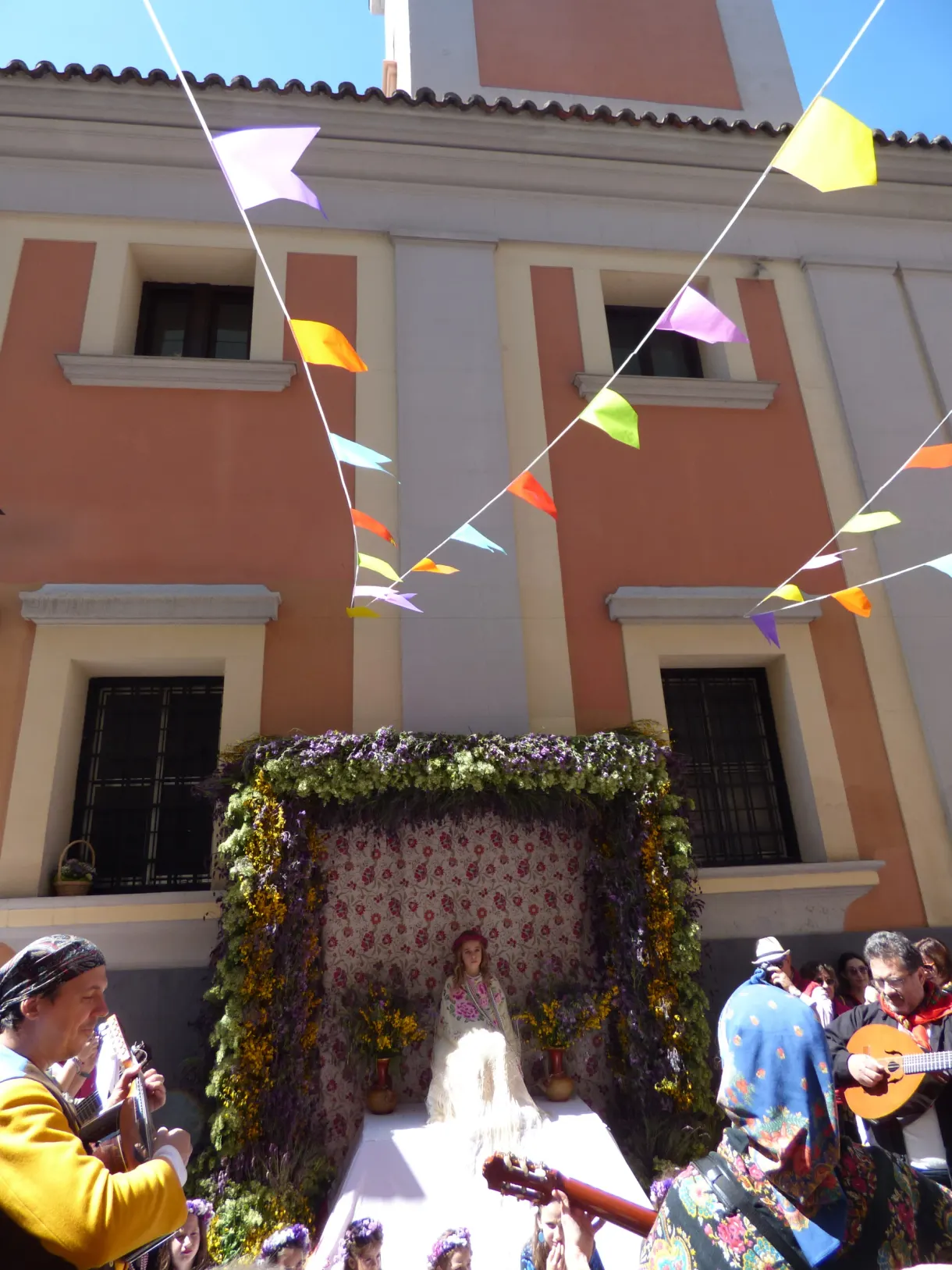 Musicians in costume in front of a flower-decked altar beneath the garlands