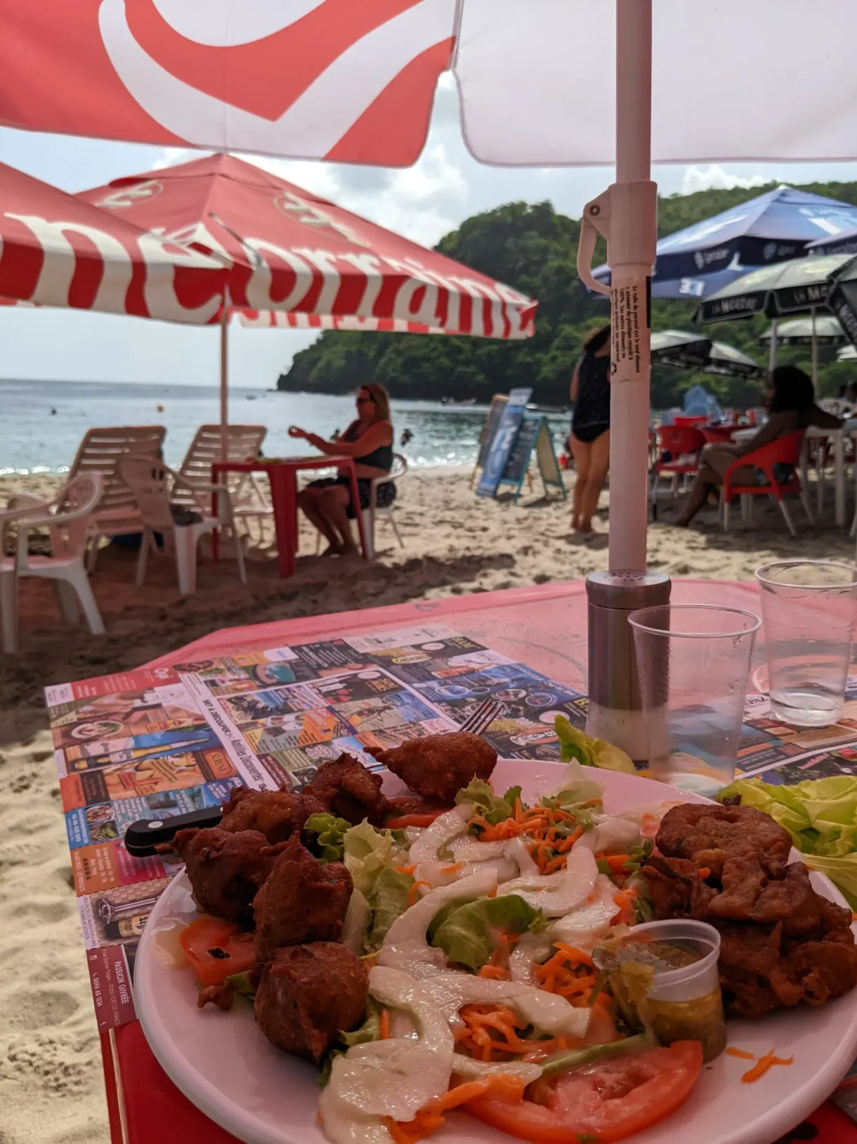 Assiette d'accras et de crudités sur une table de plage, sous un parasol rouge