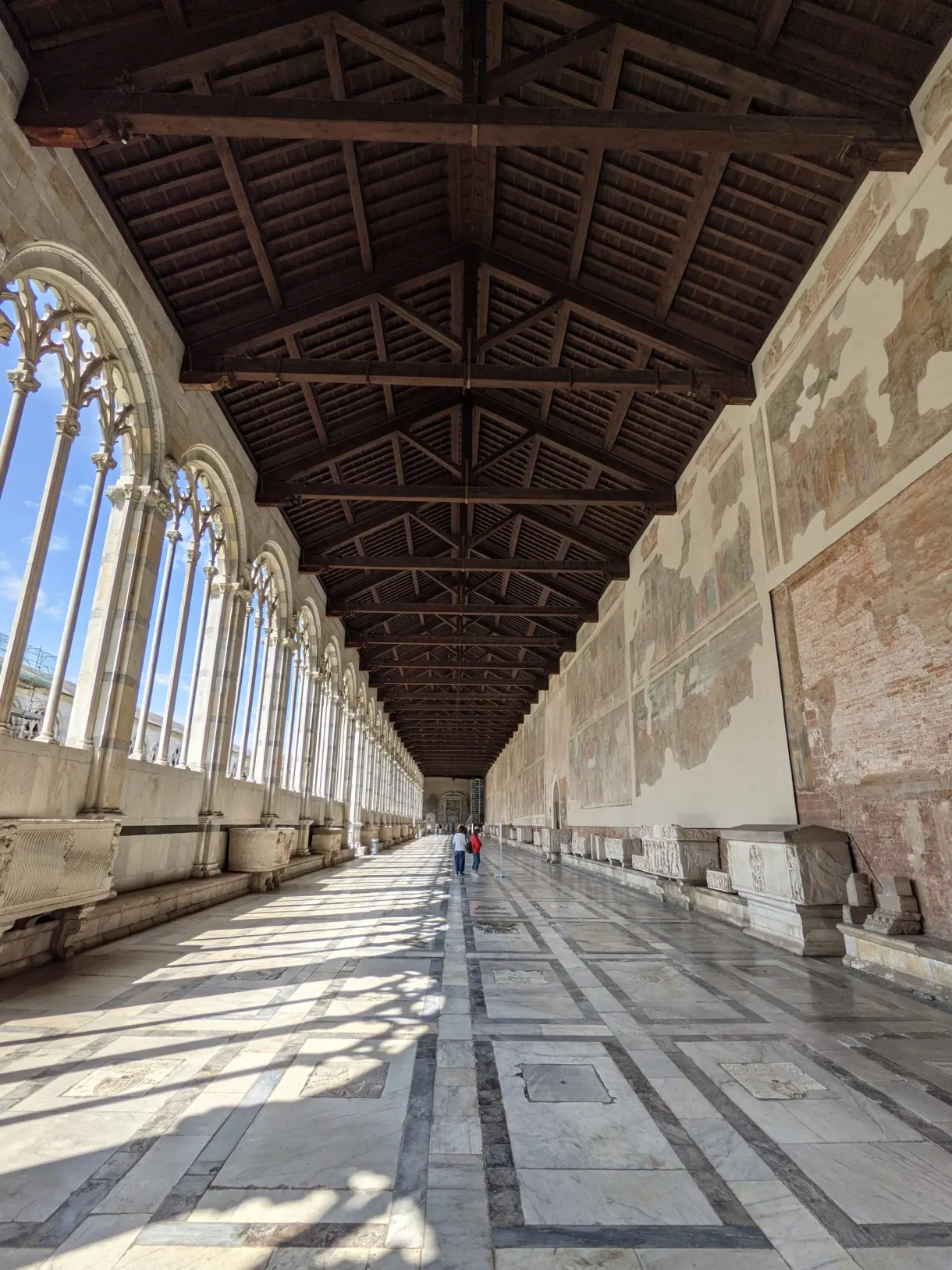 Long paved gallery of the Camposanto beneath its wooden roof frame