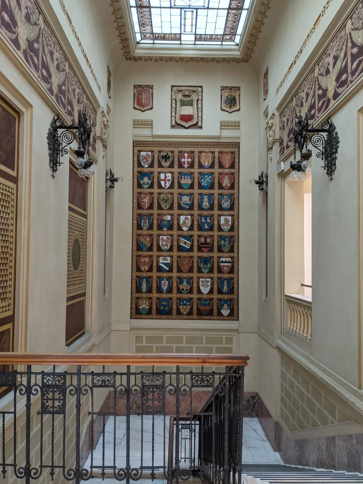 Painted coats of arms in a row above a staircase with an iron rail