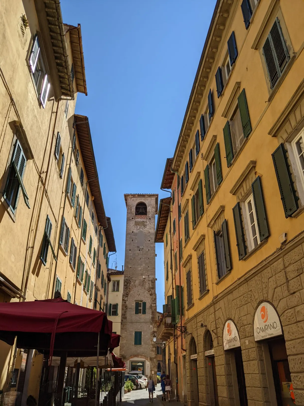 Narrow street between ochre facades, a medieval tower at the end