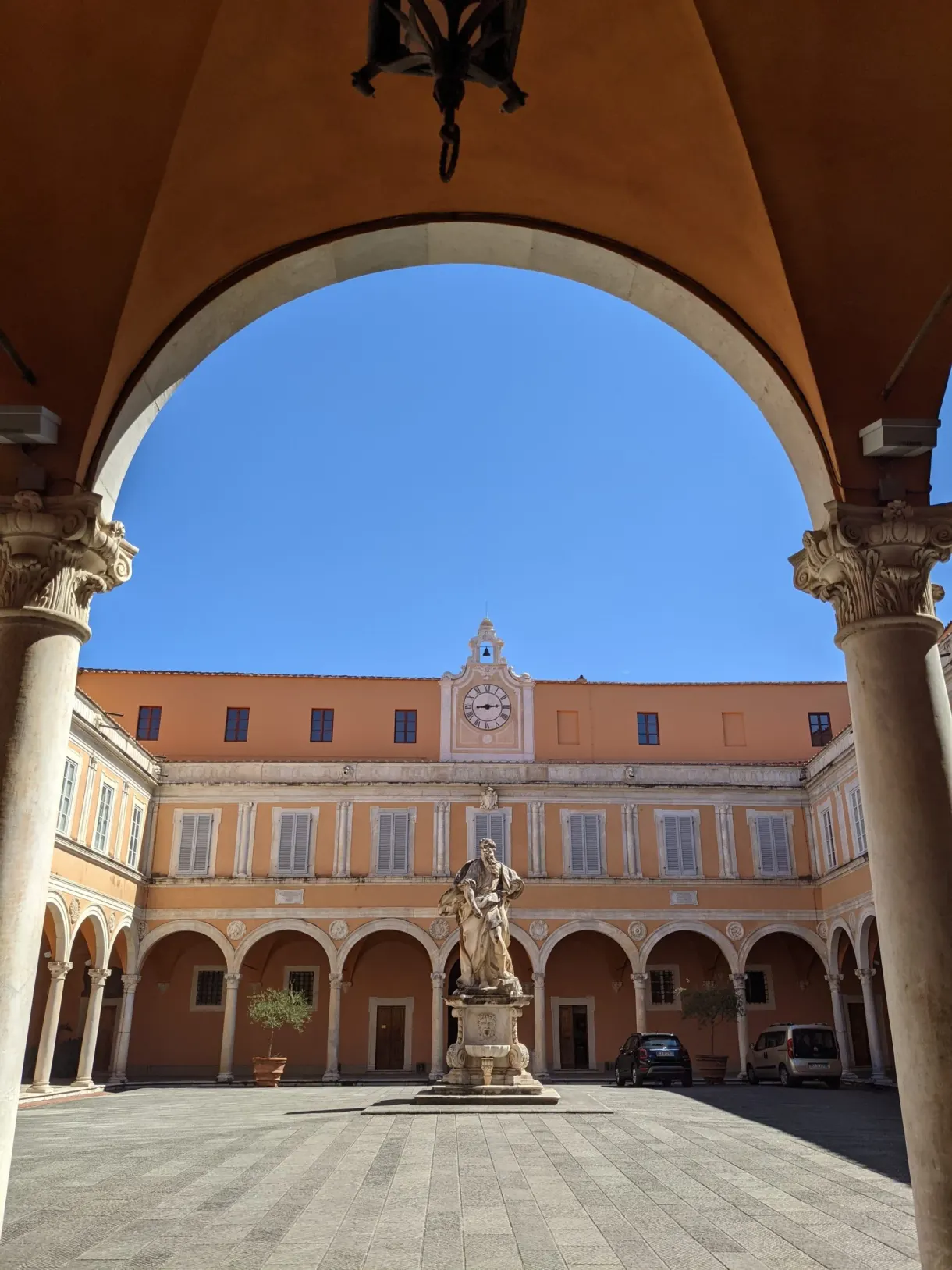 Arcade framing a courtyard with a statue and a clock
