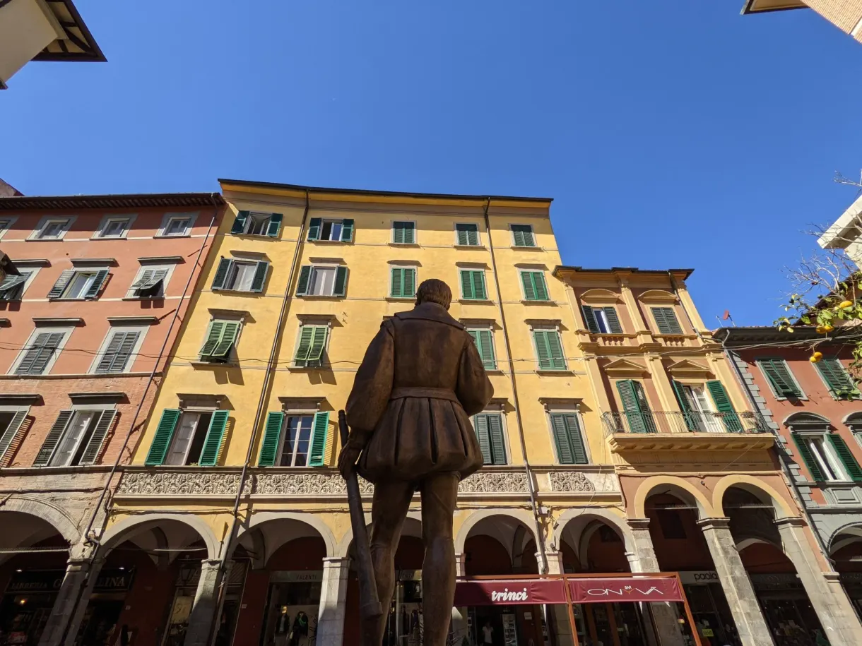 Bronze statue from behind in the middle of a colourful square