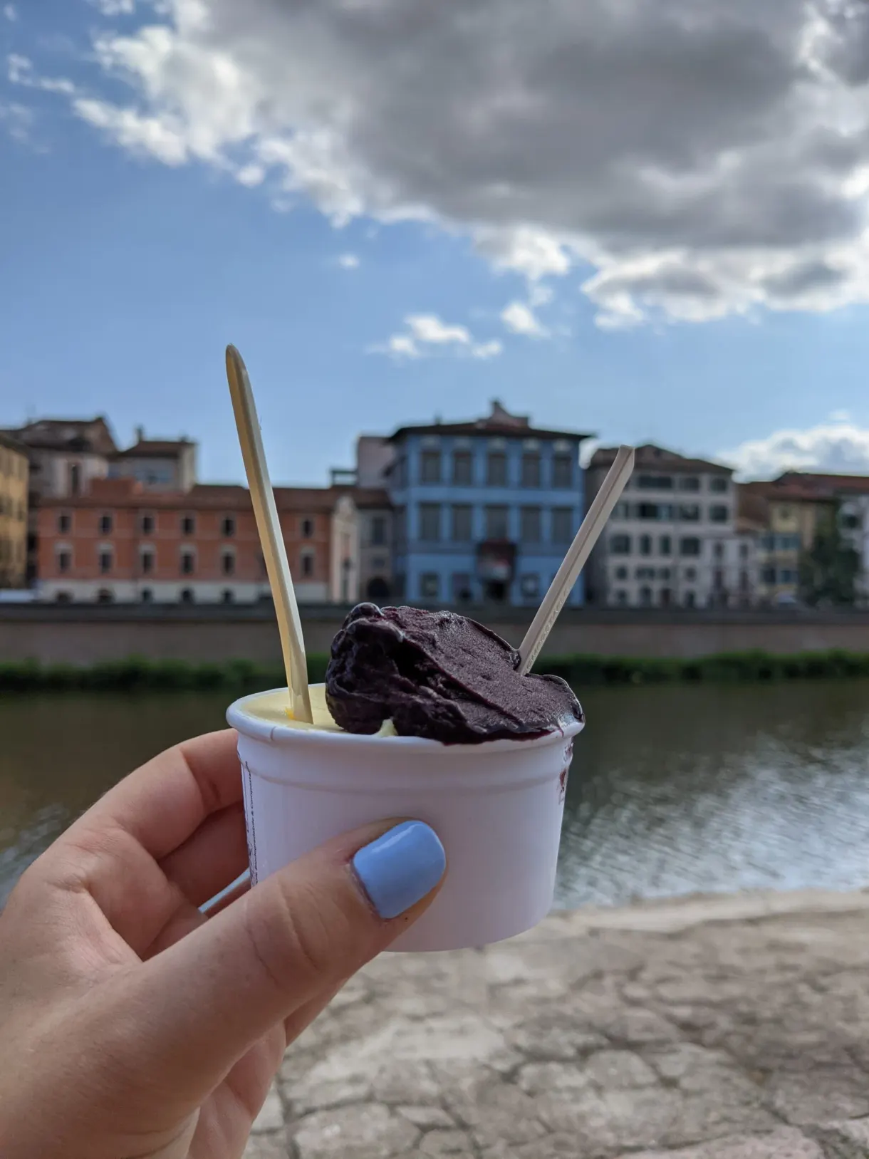 Tub of chocolate ice cream held up in front of the Arno quays