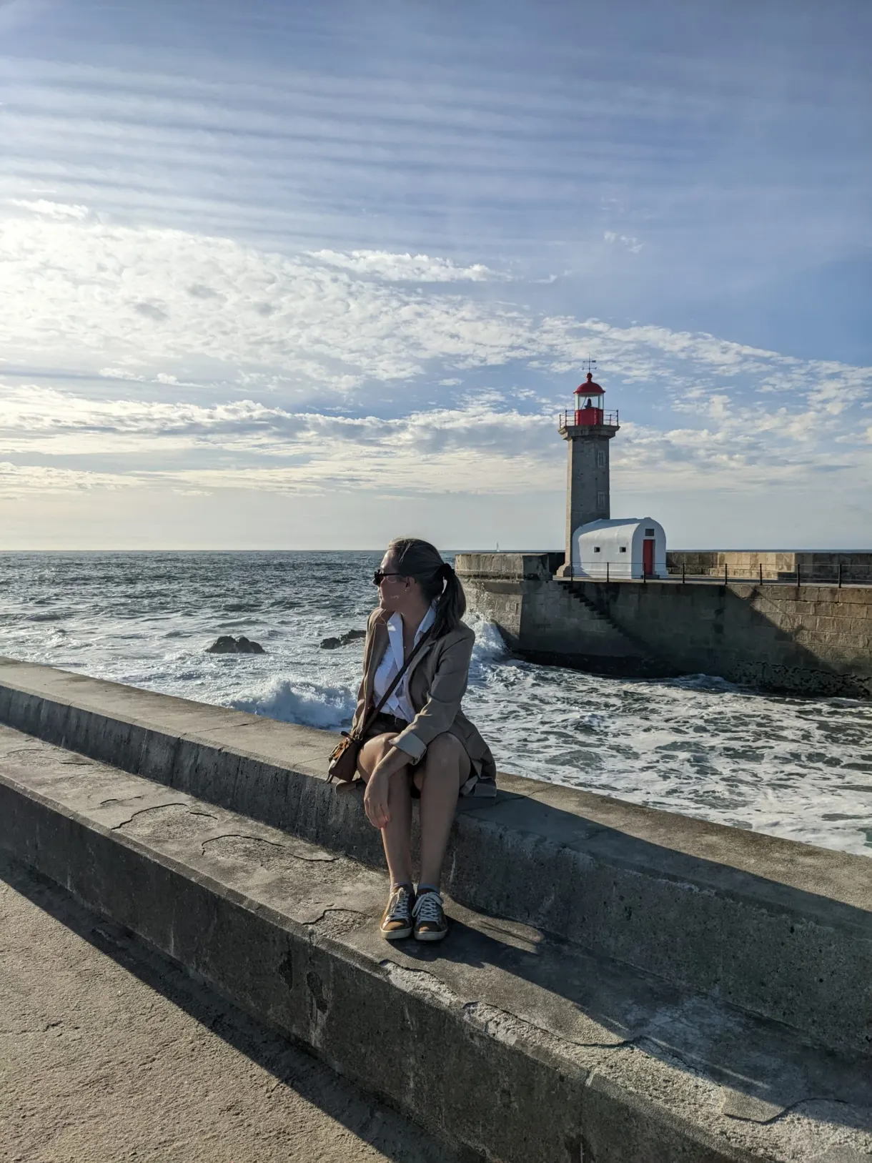 Femme assise sur la digue face au phare rouge