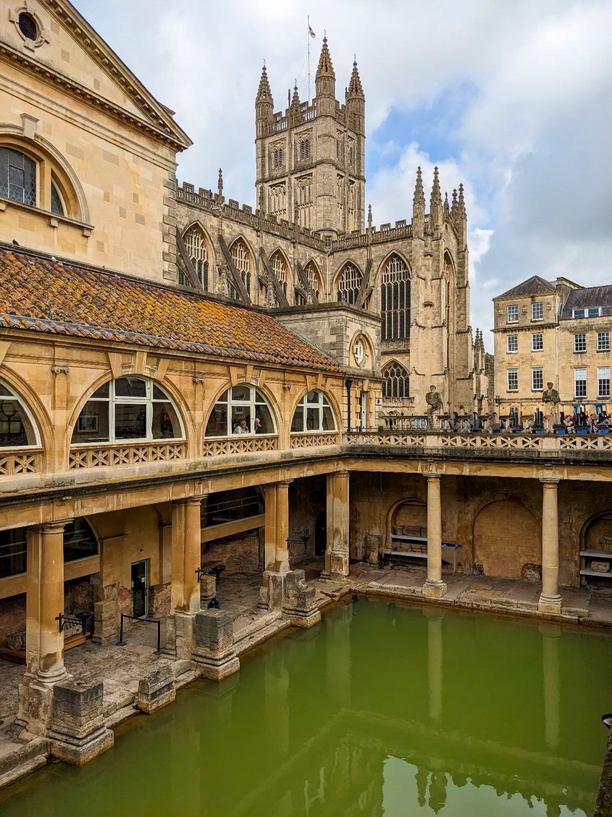 Roman Baths in Bath with green water in the sunshine, the abbey in the background