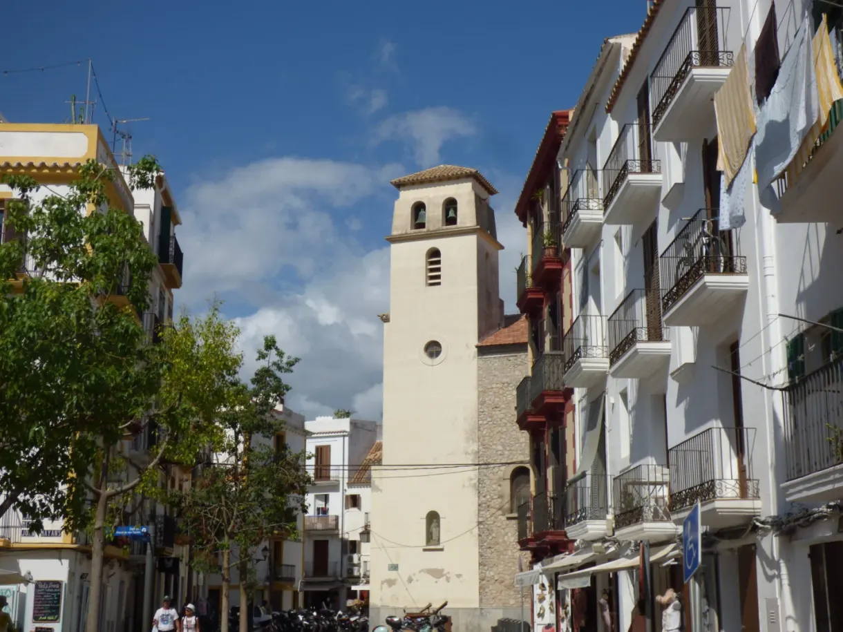 White bell tower of a church wedged between buildings