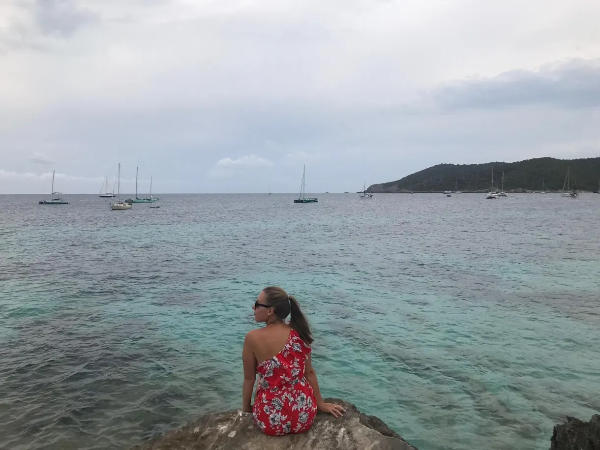 Woman in a floral dress sitting facing the sailing boats at anchor