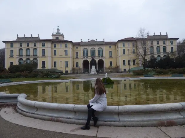 Villa néoclassique derrière son bassin, femme assise sur la margelle