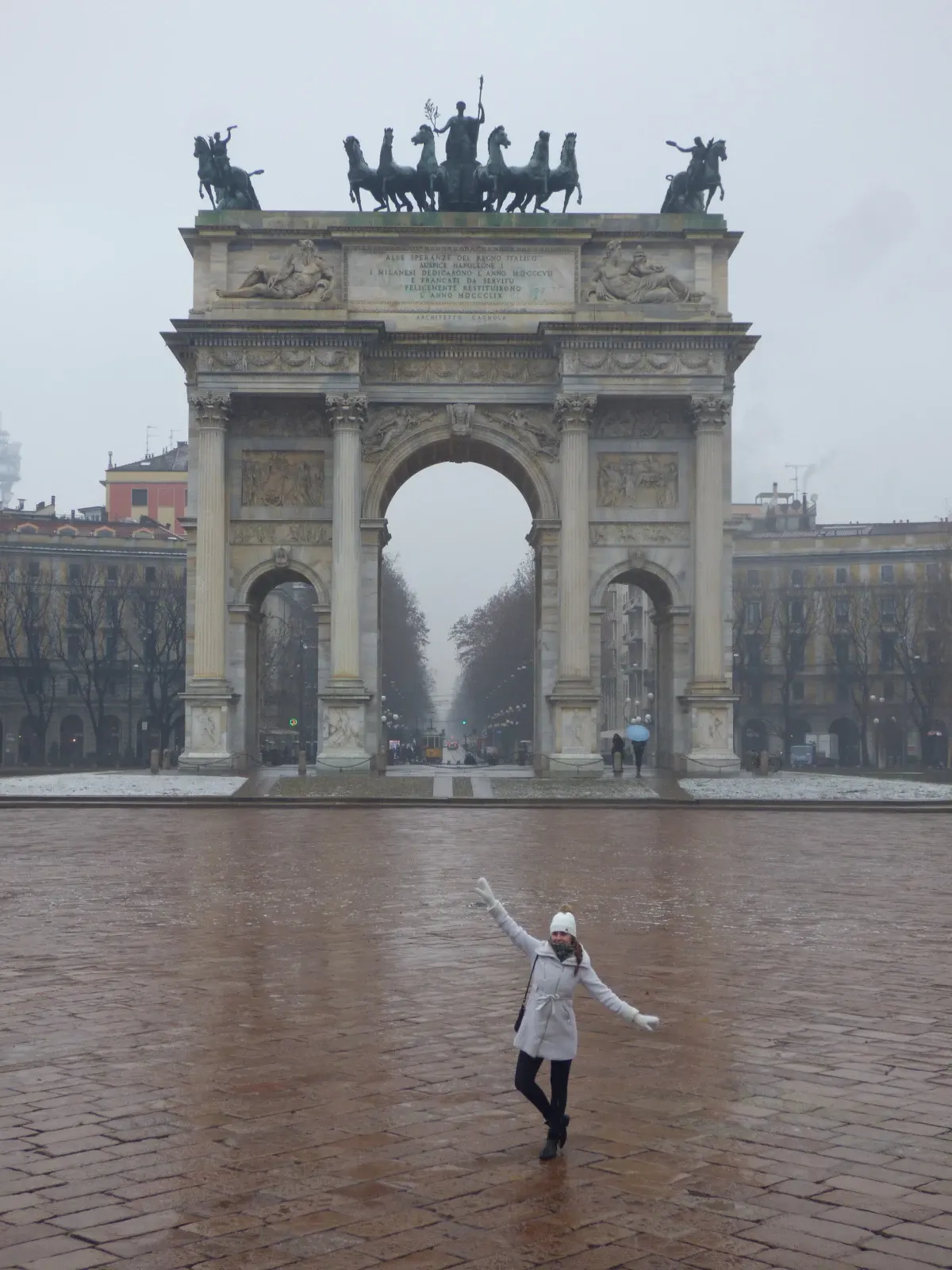 Arc de la Paix et femme bras écartés sur le pavé mouillé