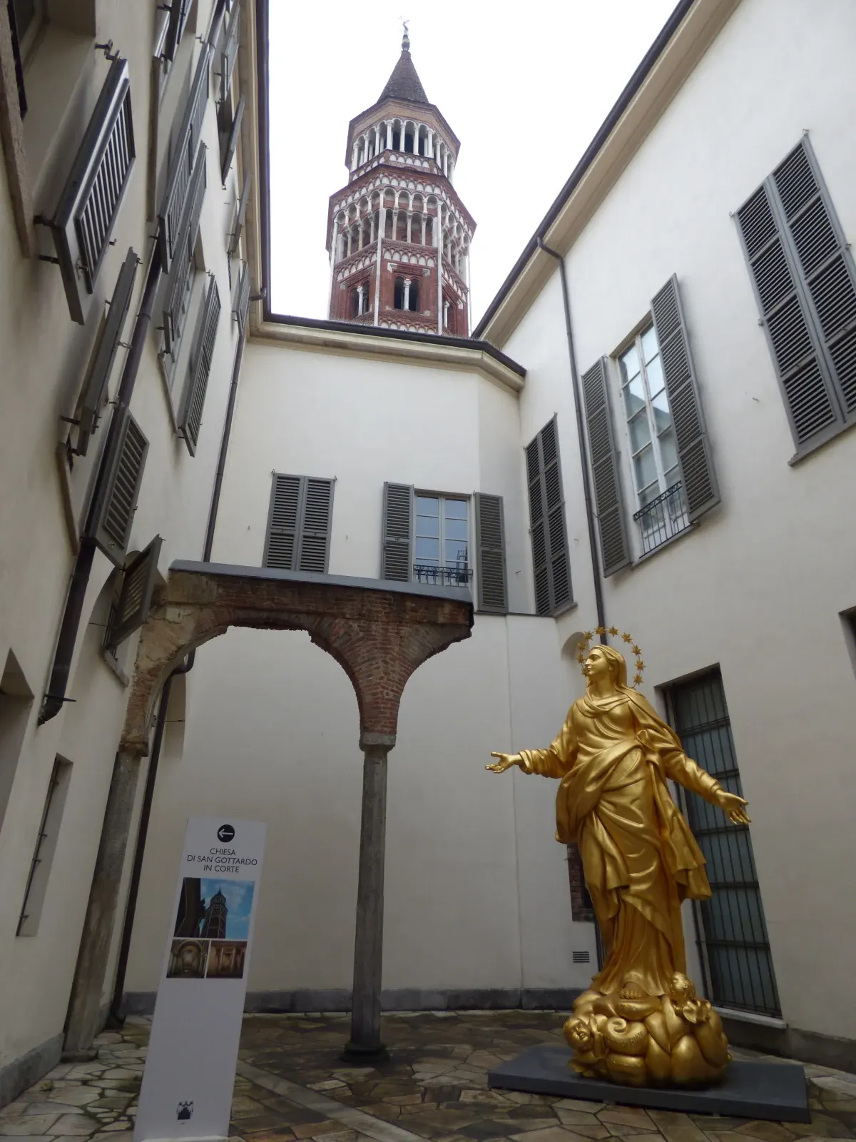 Statue dorée de la Vierge dans une cour, campanile de brique