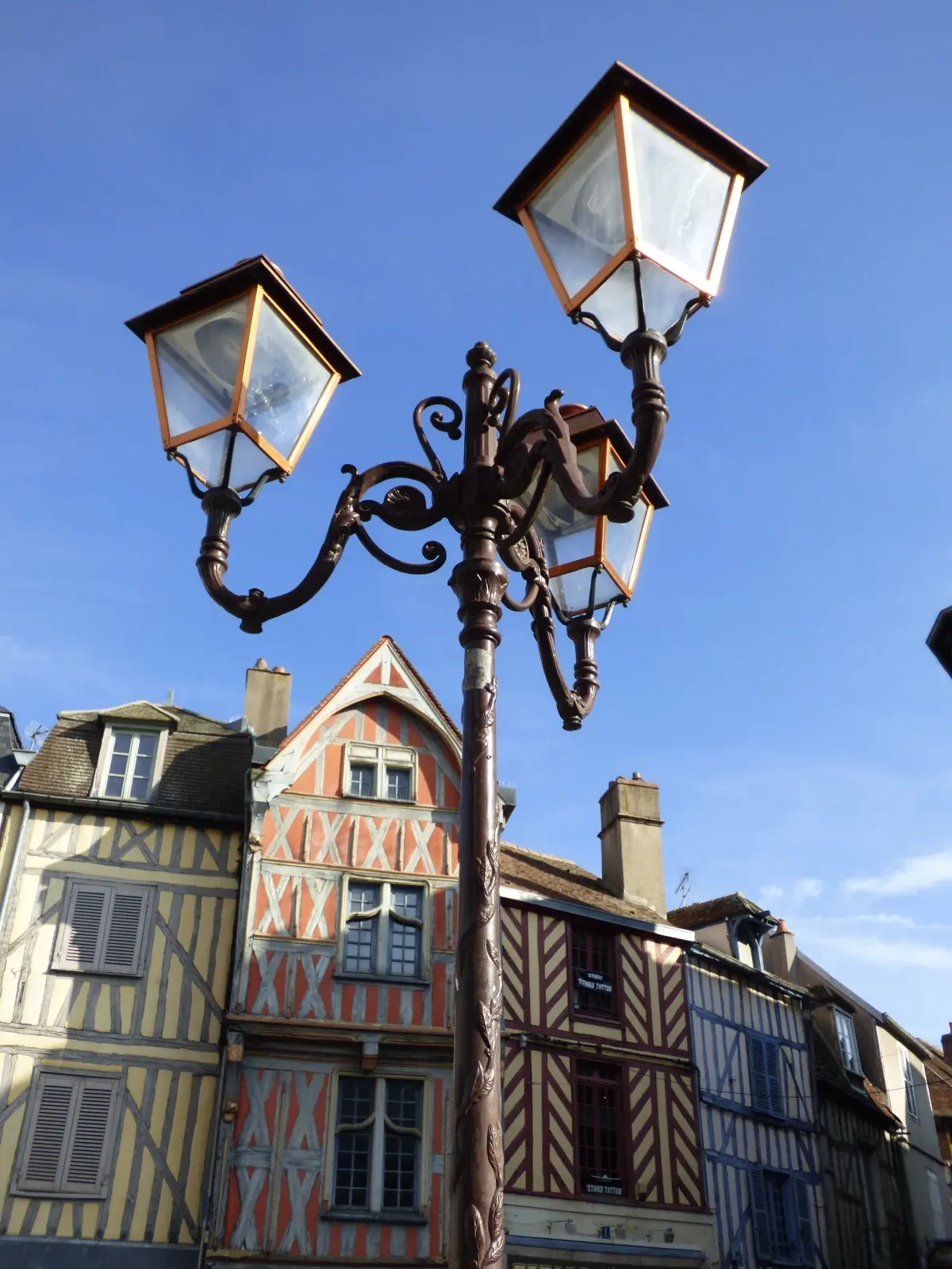 Ornate street lamp in front of half-timbered houses in Auxerre