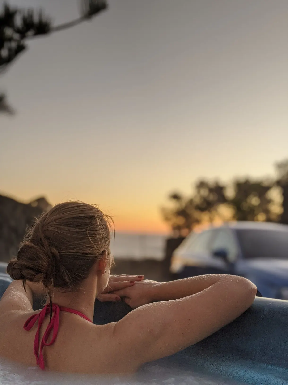 Woman seen from behind in the hot tub facing the setting sun