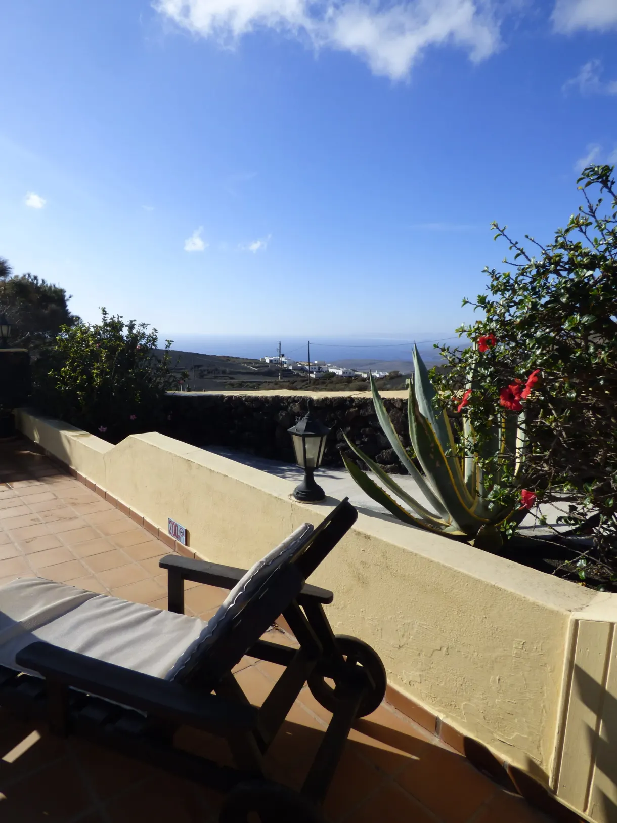 Sun lounger on a terrace with a yellow wall, cacti and the sea in the distance