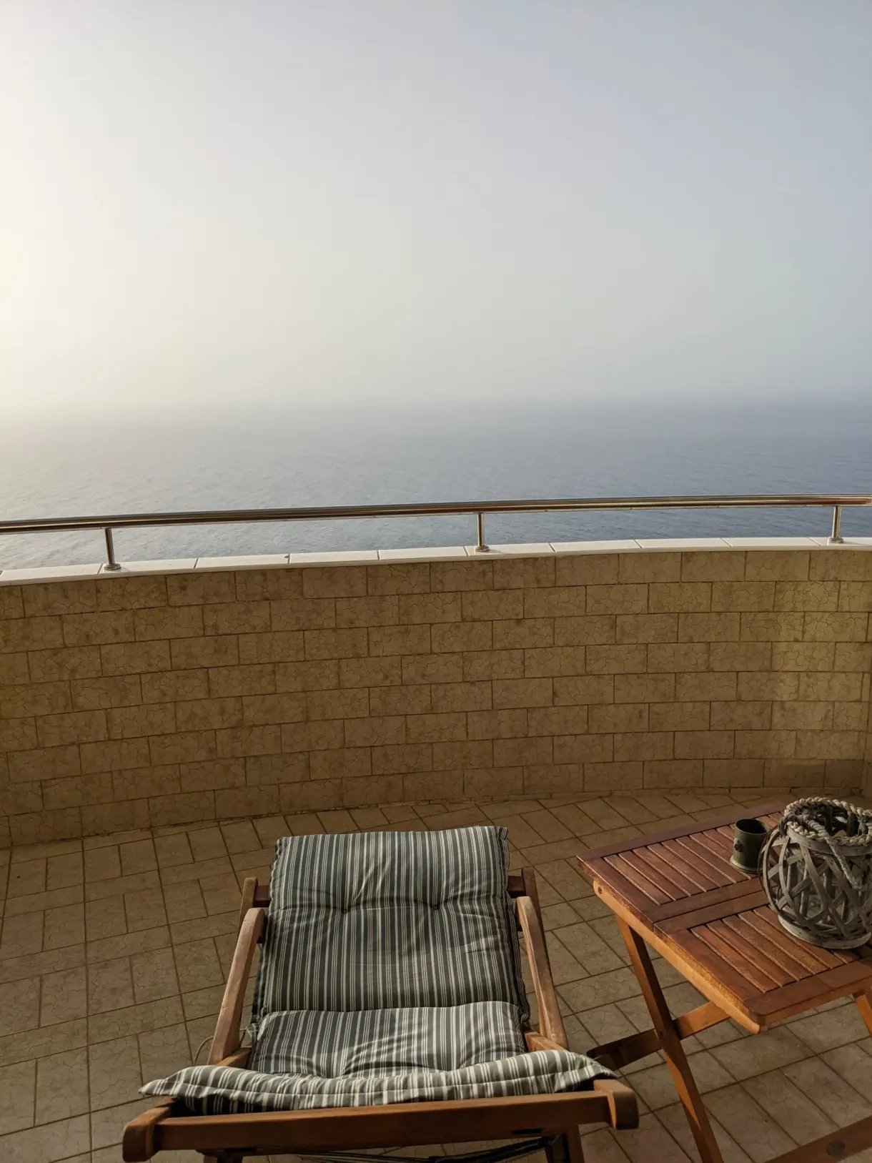 Chaise longue en bois sur un balcon arrondi face à la mer