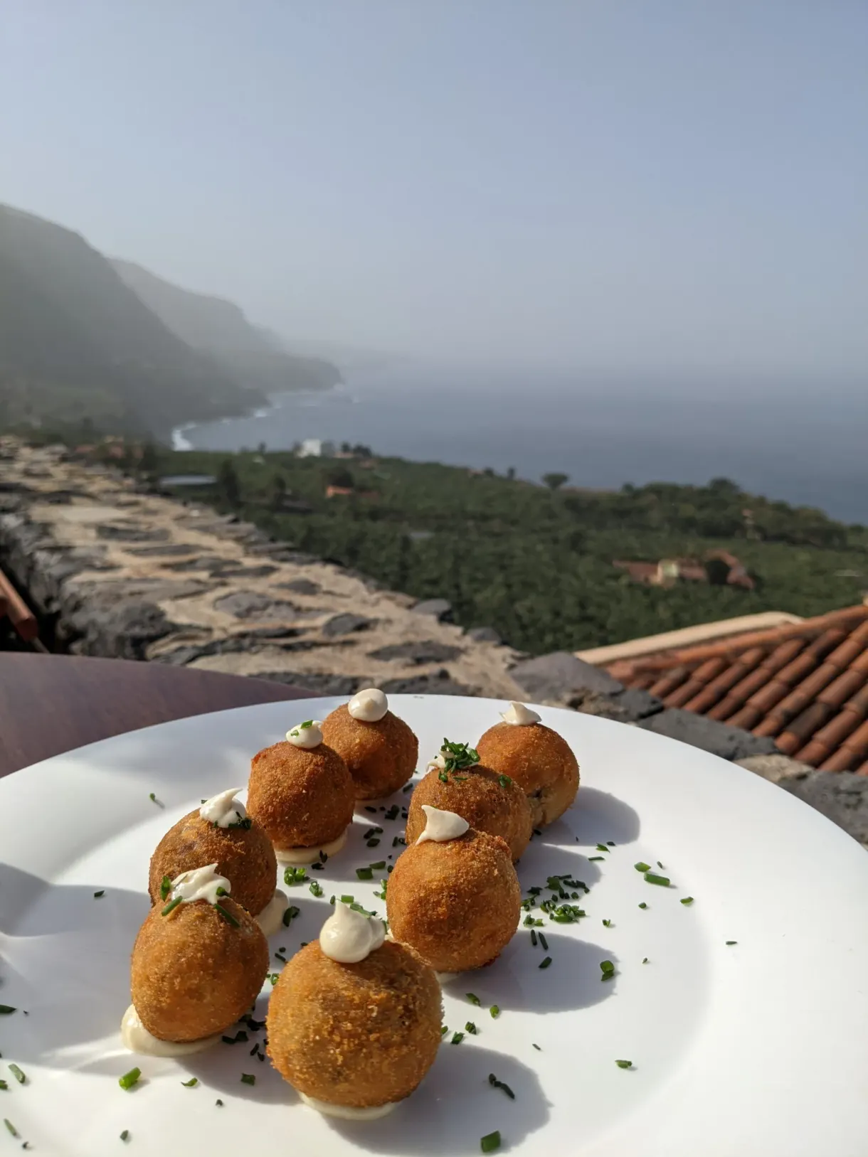 Croquettes dressées en assiette blanche devant la côte brumeuse
