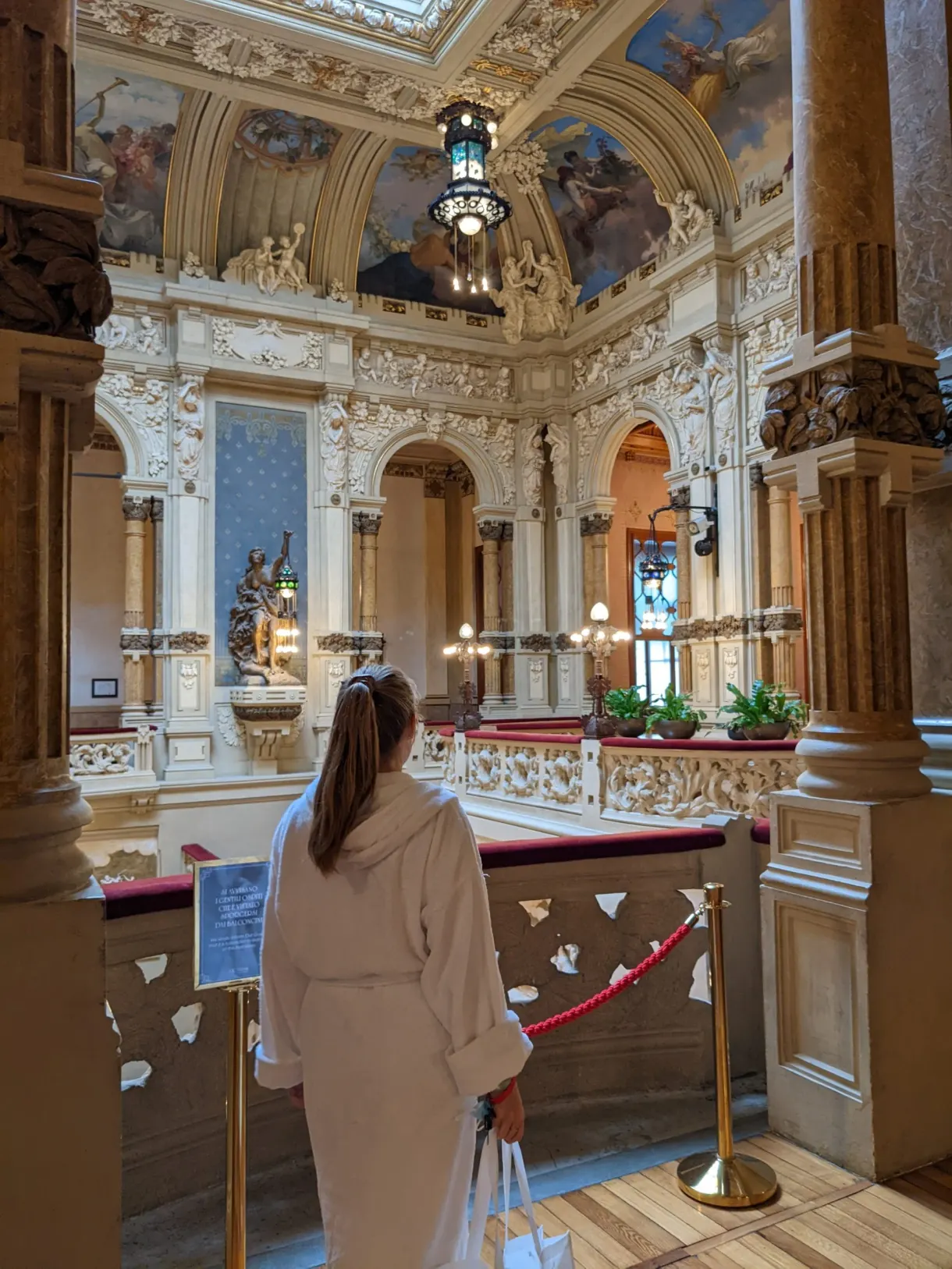 Femme en peignoir devant les stucs dorés d'un balcon