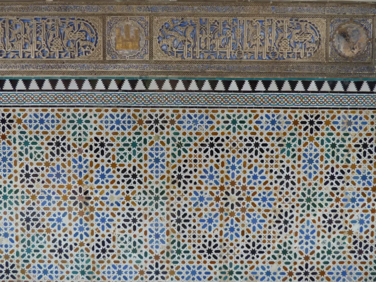 Wall of blue and ochre zellige tiles beneath a carved frieze