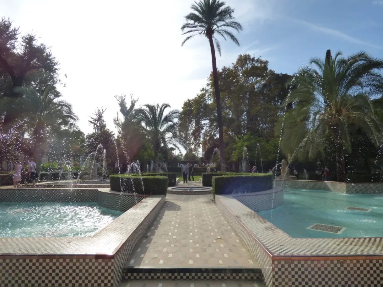 Turquoise pool and water jets between palm trees and pines