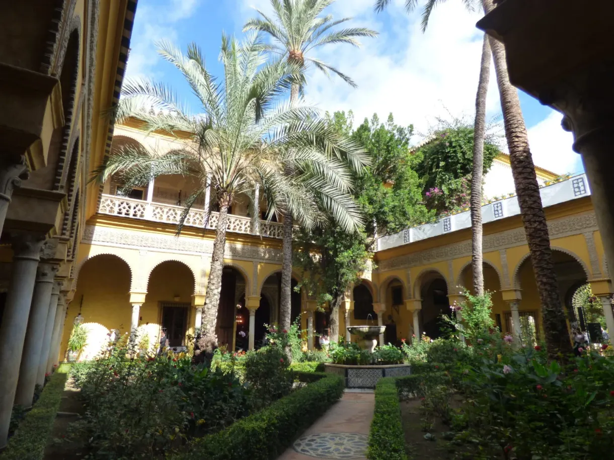 Patio with white arcades, palm trees and flower beds