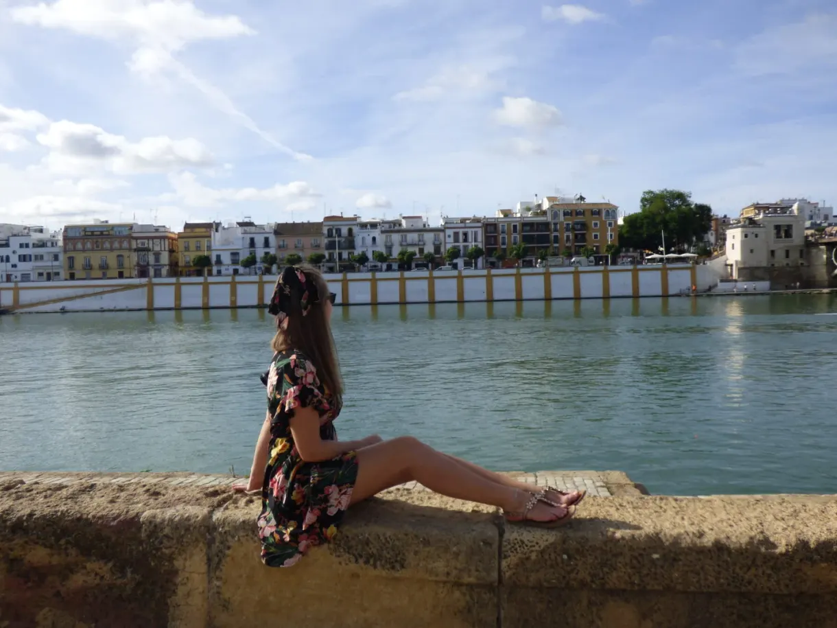 Woman sitting on a low wall facing the river and the houses