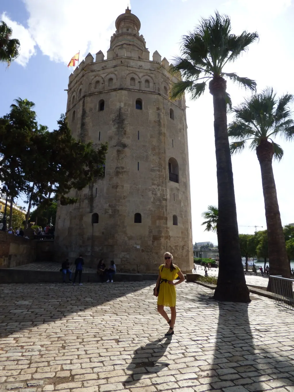 Woman in a yellow dress in front of the golden tower and two palm trees