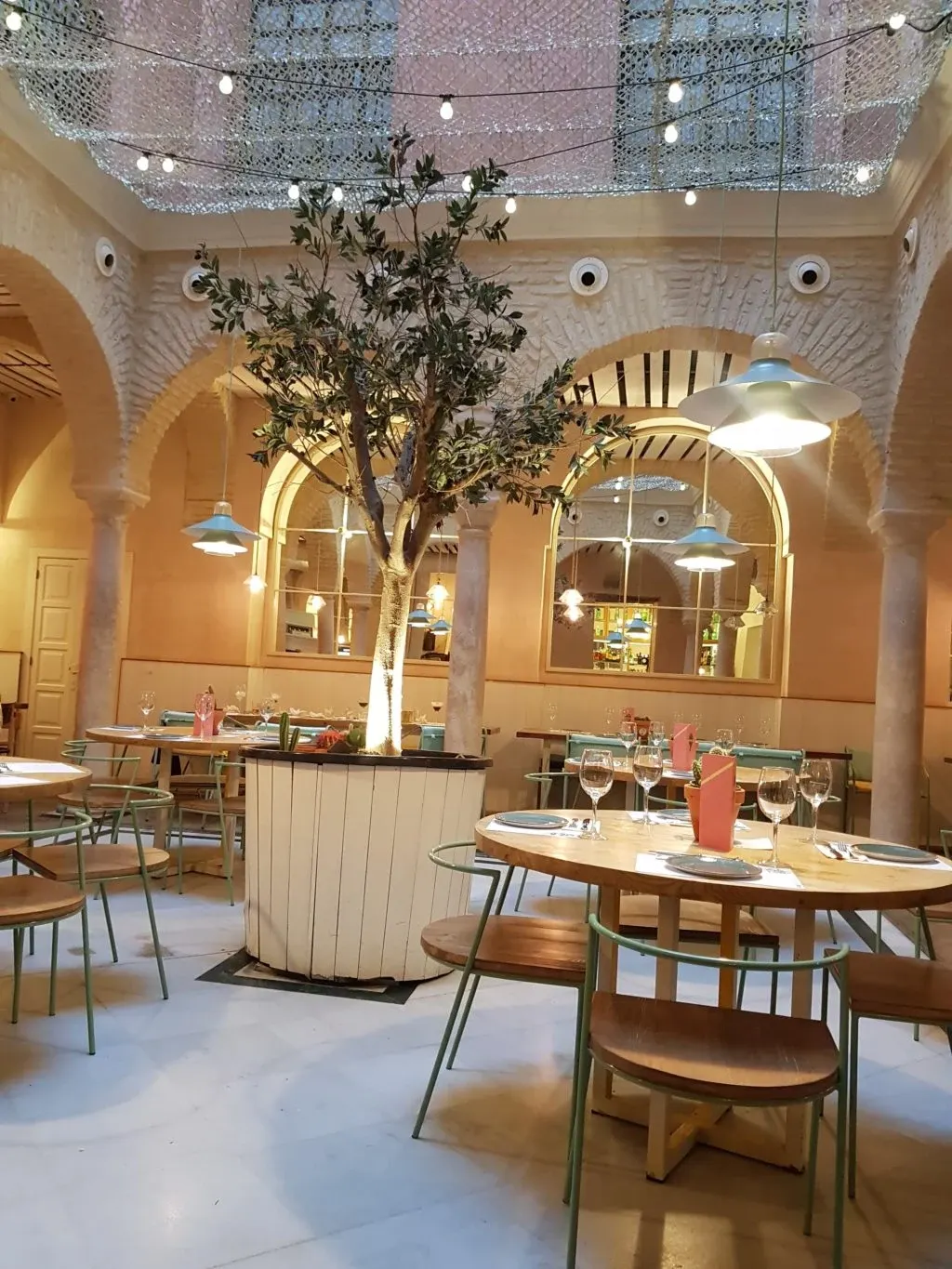 Round tables under the arcades and a potted olive tree