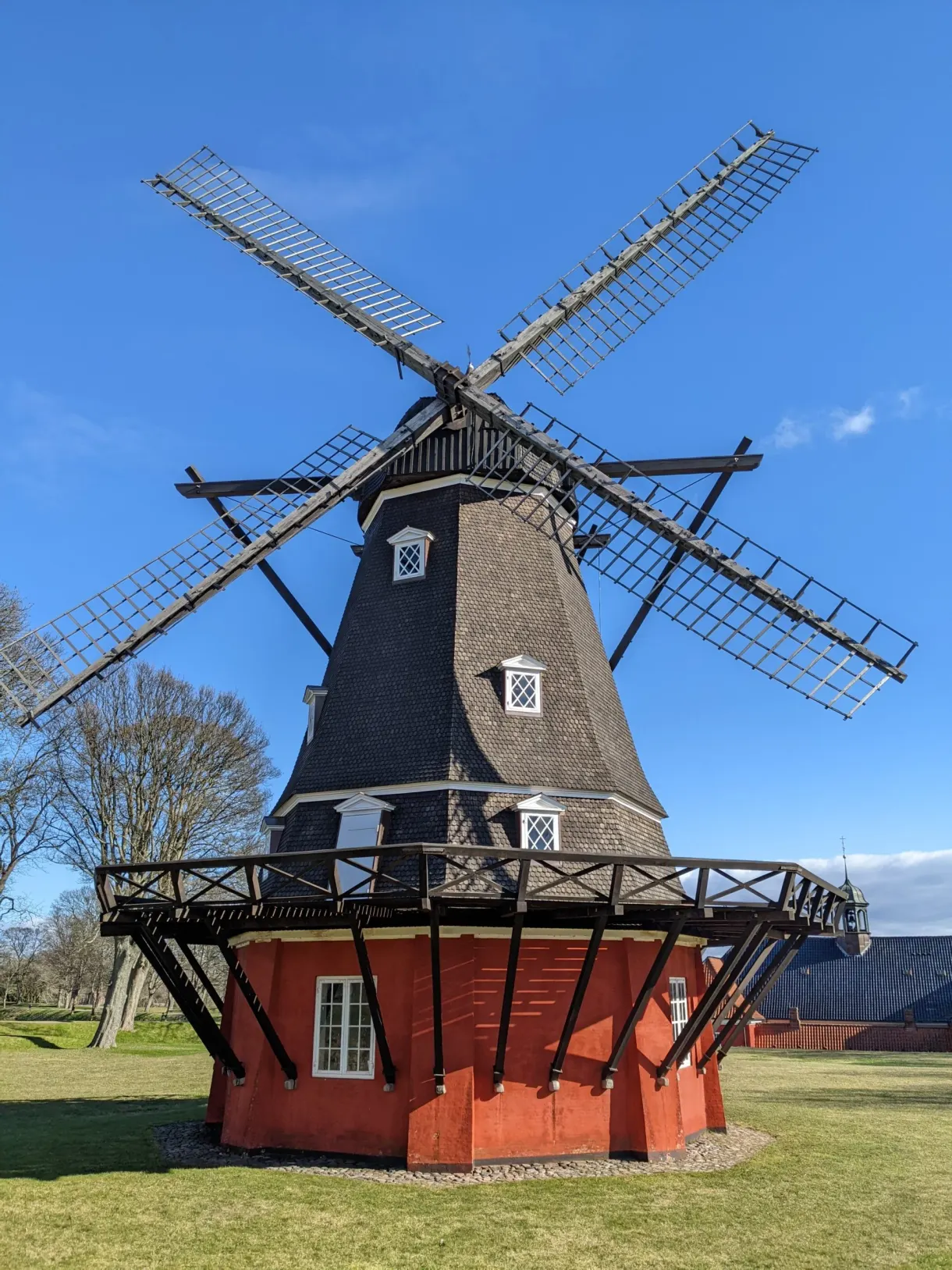 Moulin noir sur soubassement rouge, ailes de bois déployées