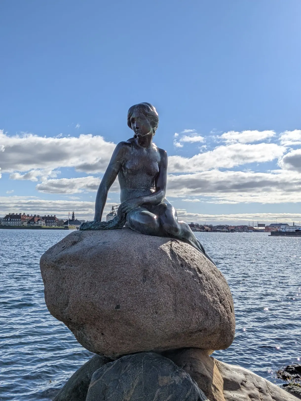 Statue de la Petite Sirène assise sur son rocher face au port