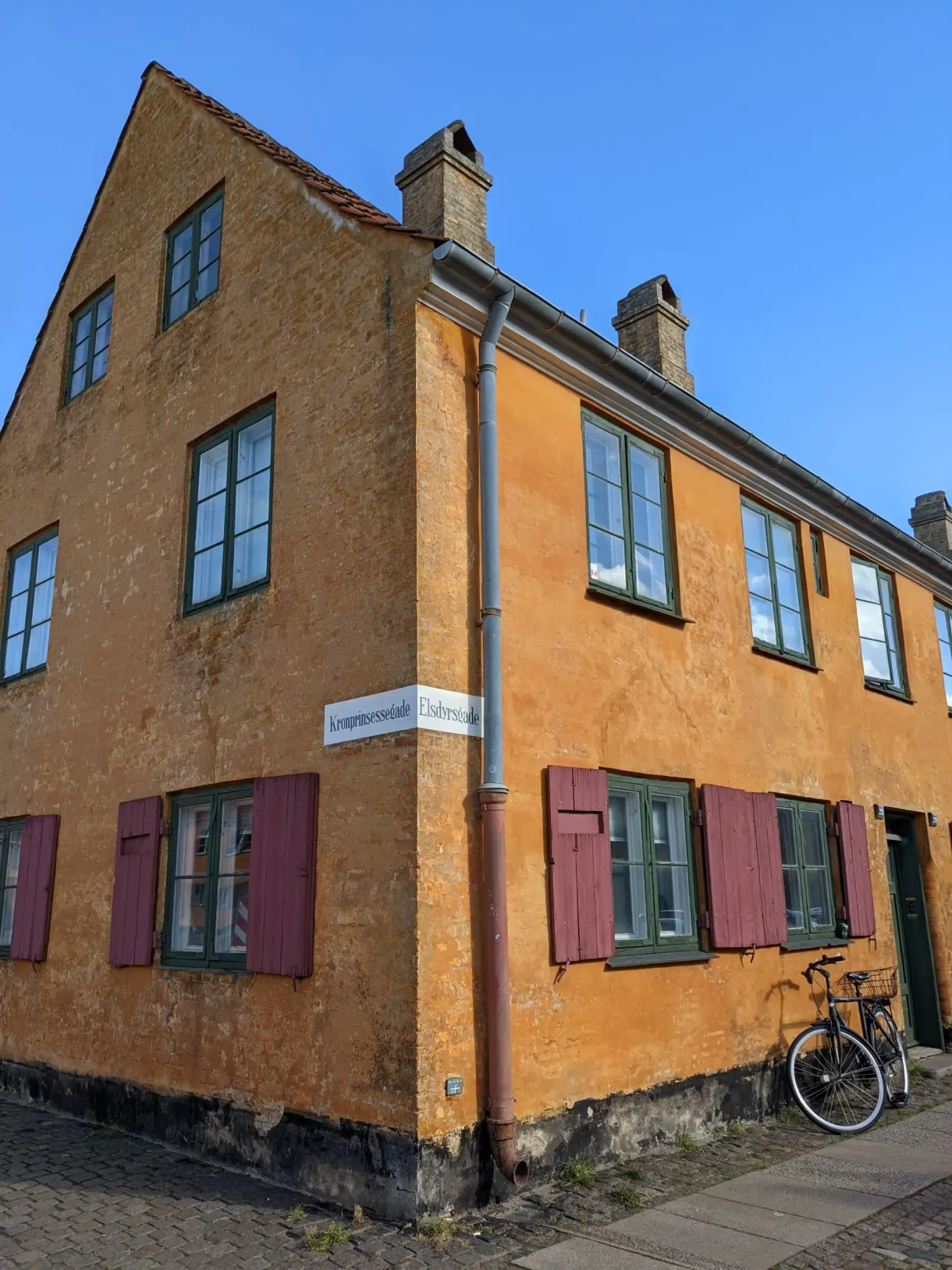 Maison d'angle jaune à plaque de rue, vélo appuyé contre le mur