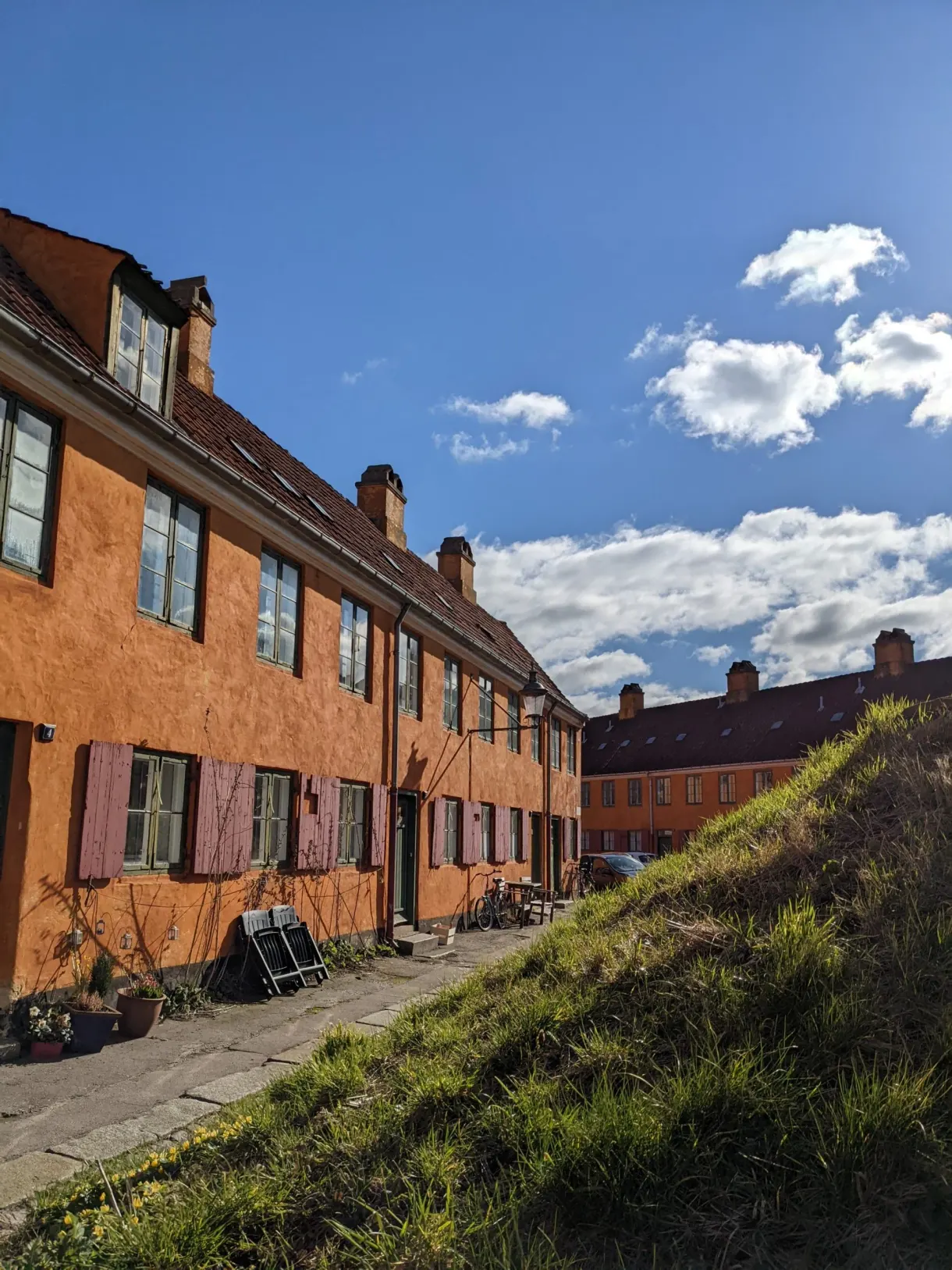 Talus herbeux longeant les petites maisons ocre aux volets roses